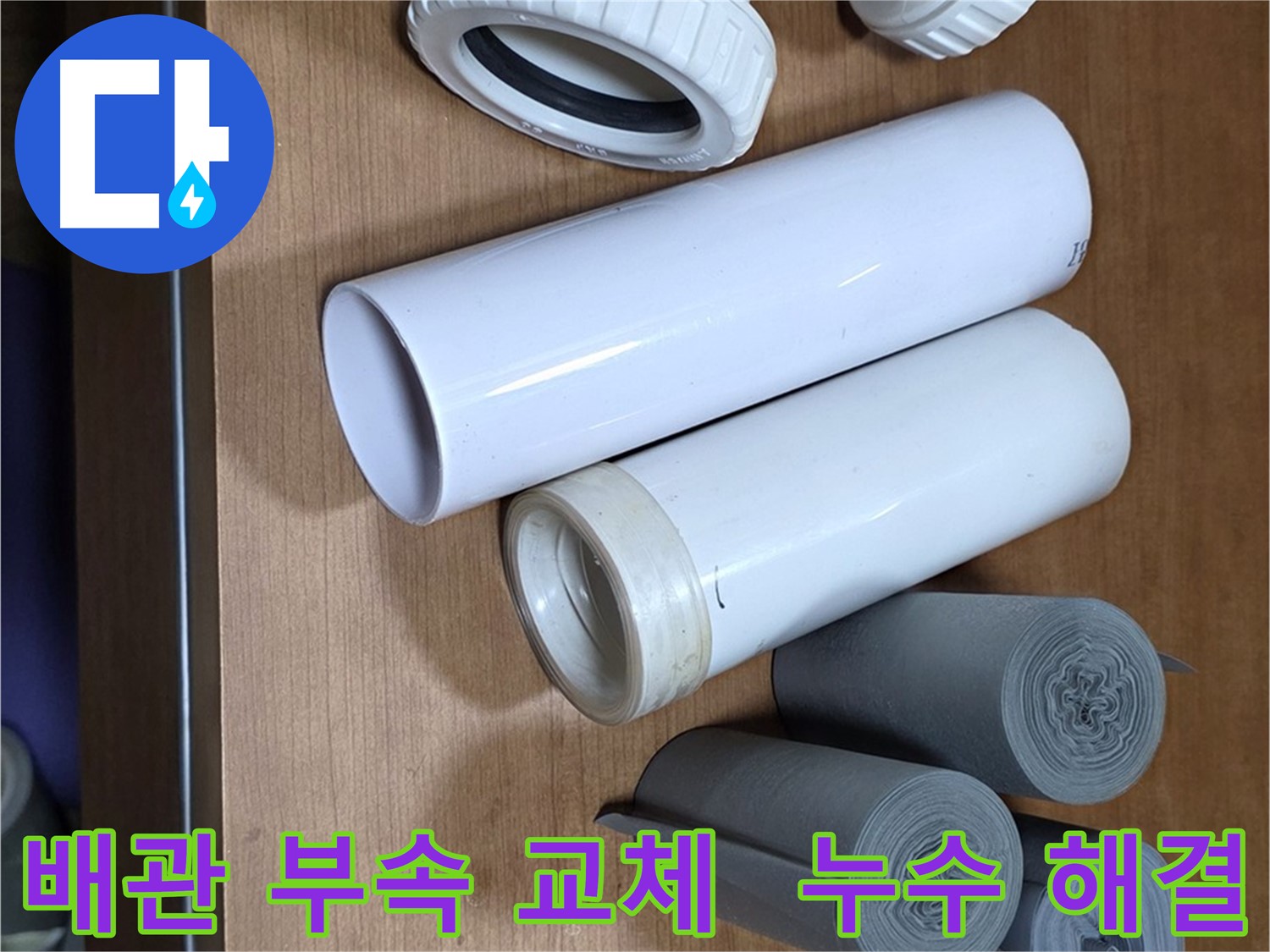 누수 해결을 위해 준비된 다양한 배관 부속 - T자관, 엘보, 소켓과 누수 방지 테이프가 놓여 있습니다.