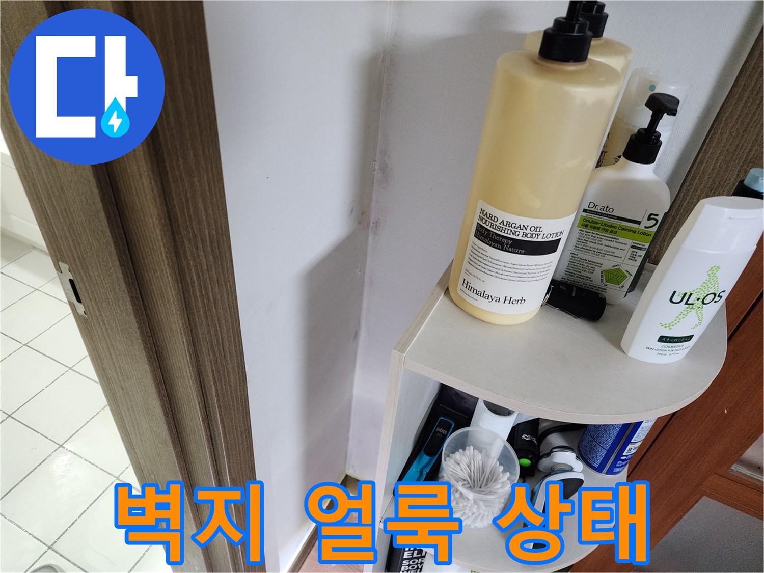 화장품 선반 뒤쪽 벽지에 나타난 누수 흔적과 변색 부위