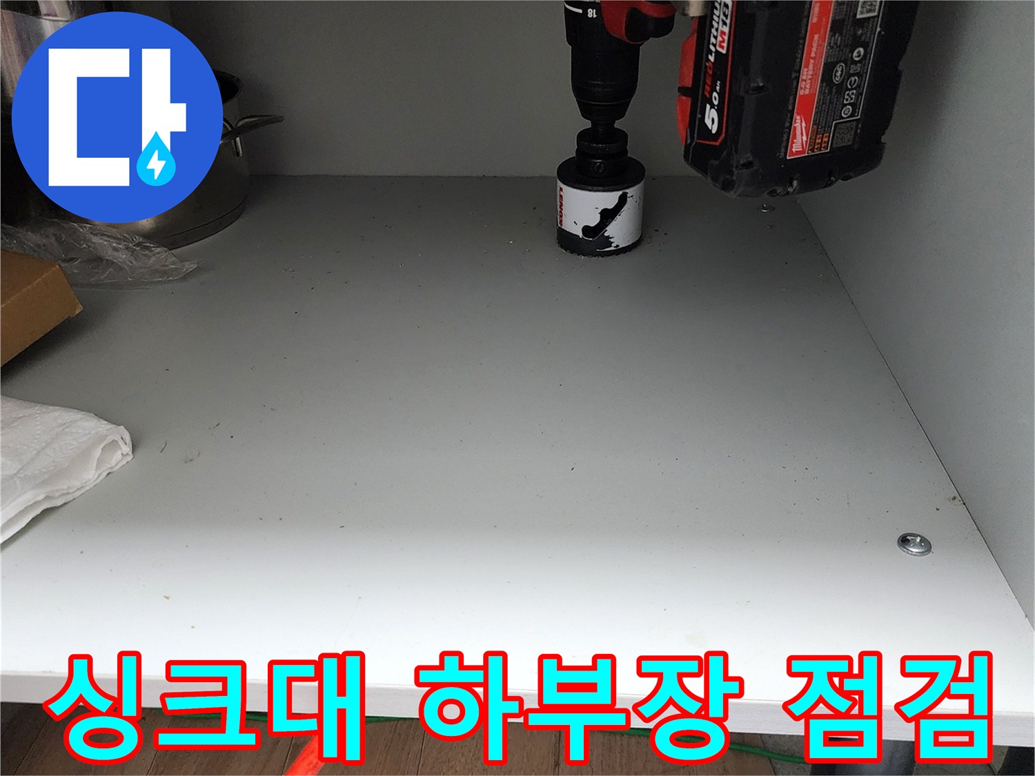주방 싱크대 하단 선반 위 전동 드릴과 조리 도구 모습