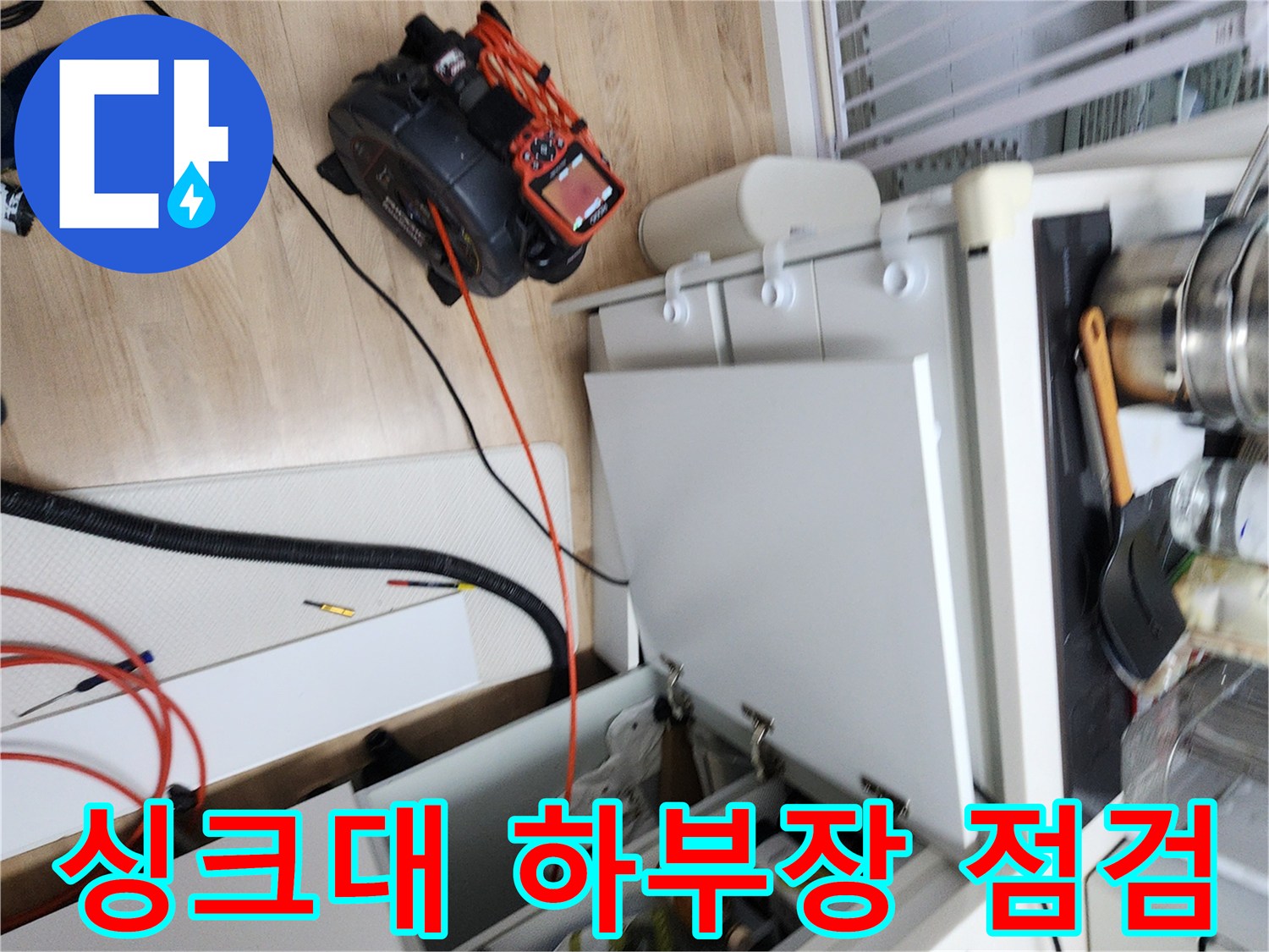 주방 싱크대 하부장을 열고 배관 상태를 점거하는 모습입니다.