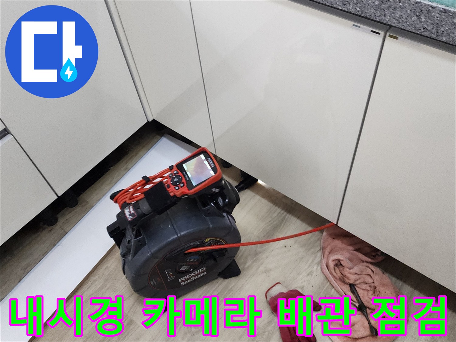 싱크대 하단 공간에서 배관 내부를 조사하기 위해 내시경 장비를 조작하는 장면입니다.