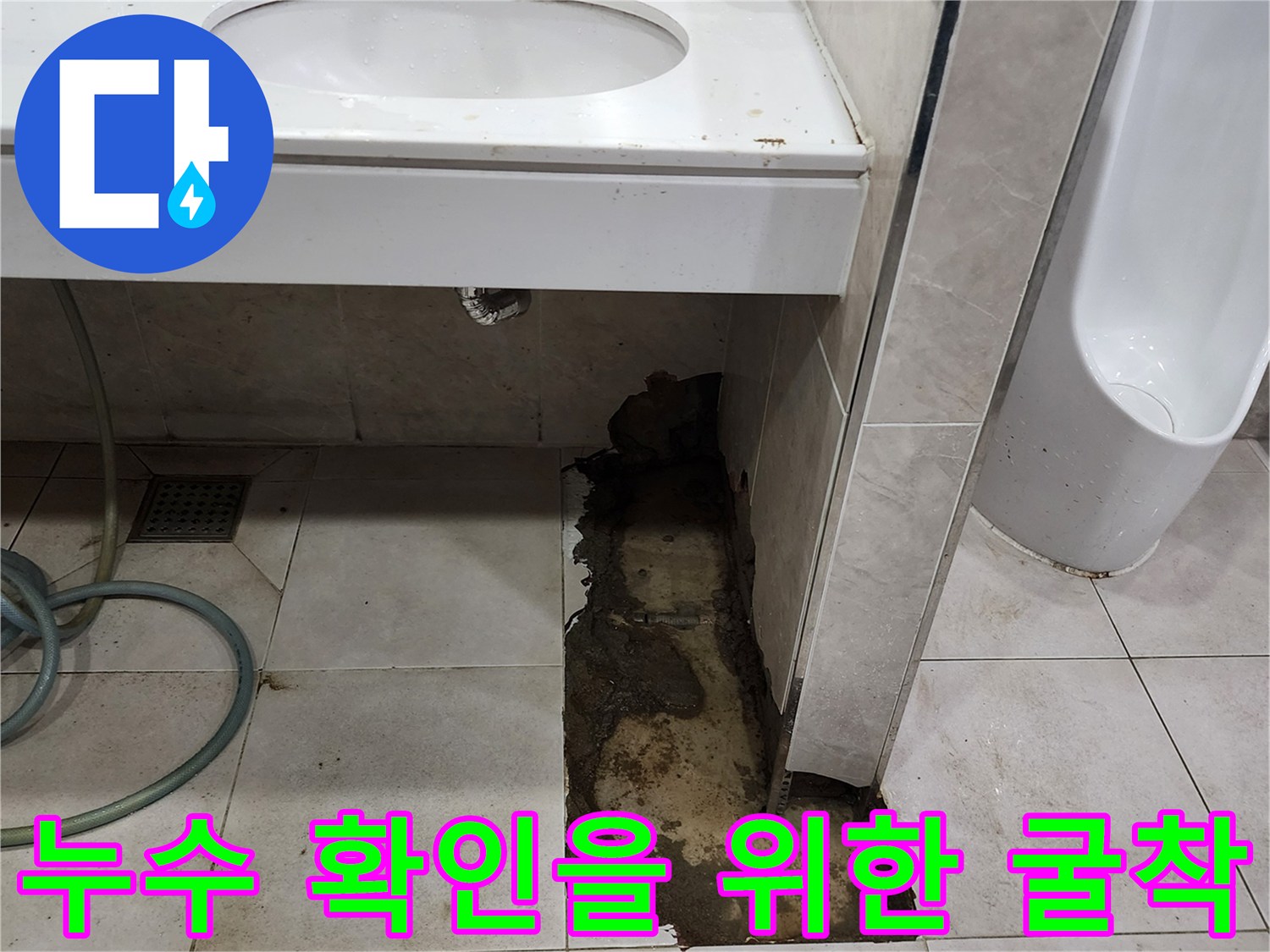 소변기 옆 타일을 제거하고 드러난 젖은 바닥면과 배관 주변의 모습입니다.