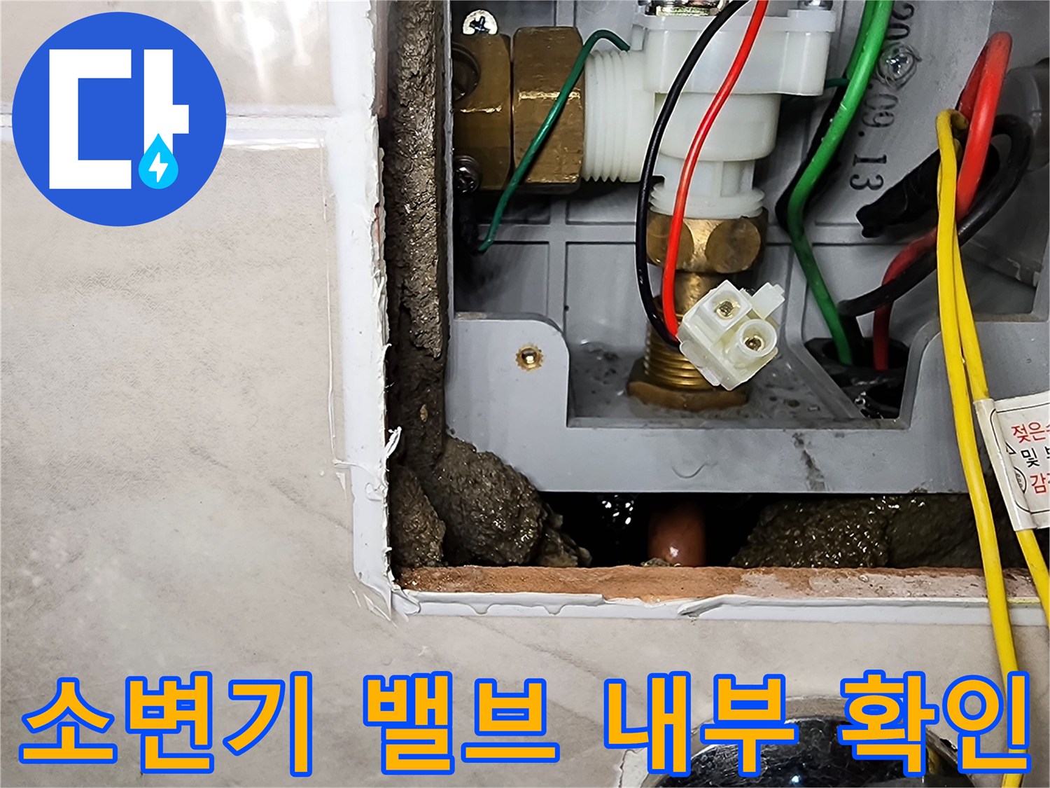 타일 안쪽 공간에 노출된 소변기 급수용 자동 밸브와 연결 부속의 모습입니다.