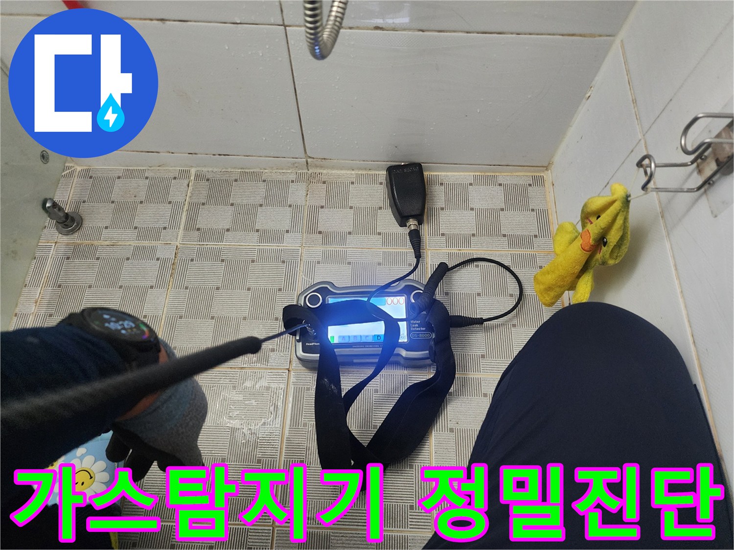 욕실 바닥에서 가스탐지기를 사용하여 배관 누수 지점을 찾는 모습입니다.
