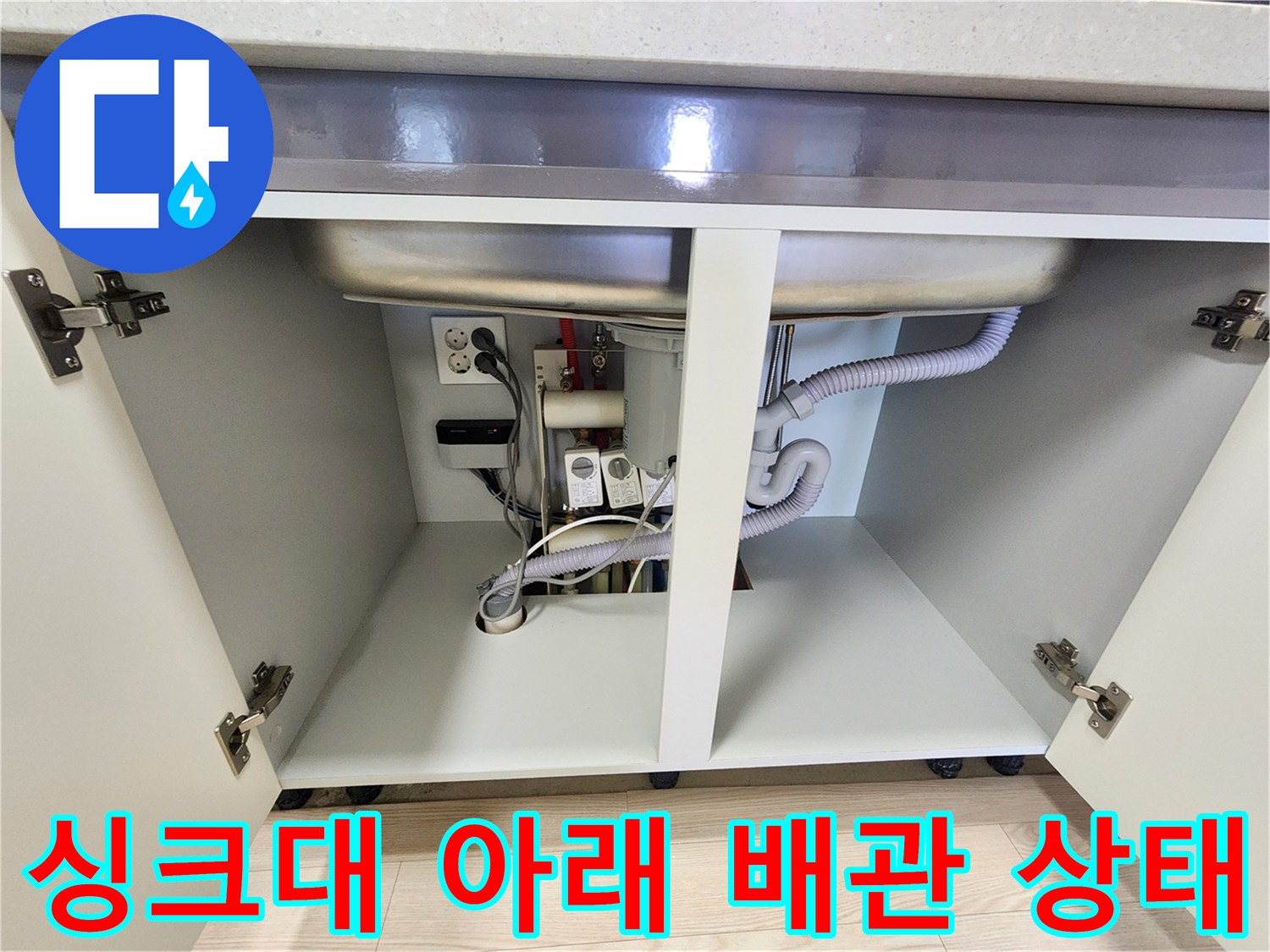싱크대 내부의 굴곡된 배수관과 전기 콘센트 및 벽면 연결부