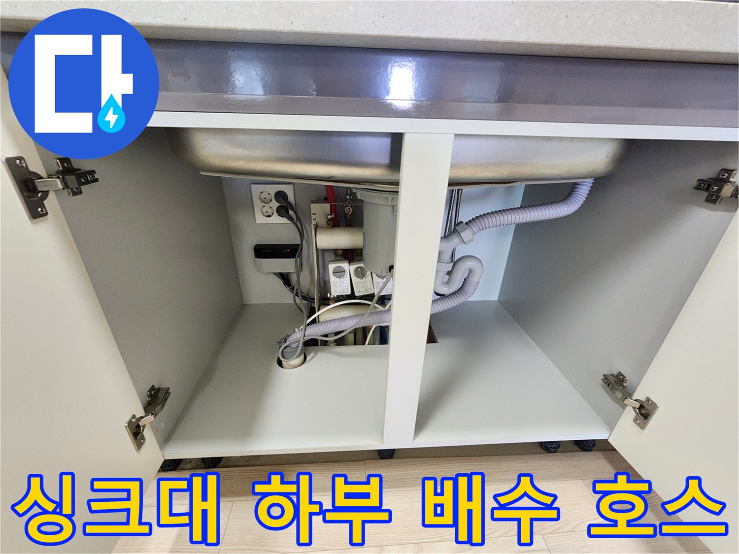 주방 싱크대 하단의 구불구불한 배수 호스와 급수 밸브 모습