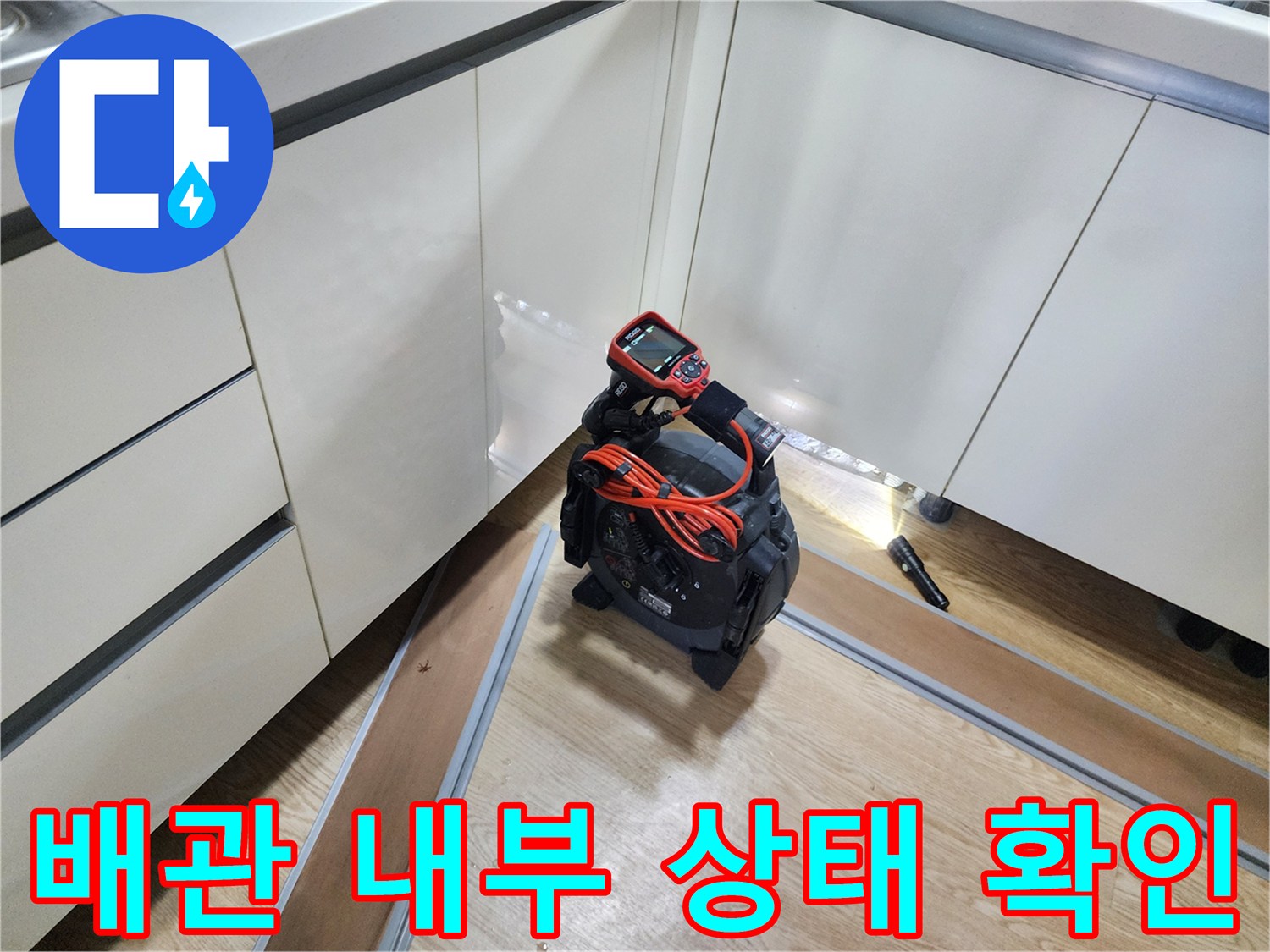 싱크대 하부장 틈새로 내시경 카메라를 넣어 배관 상태를 점검하는 모습입니다.