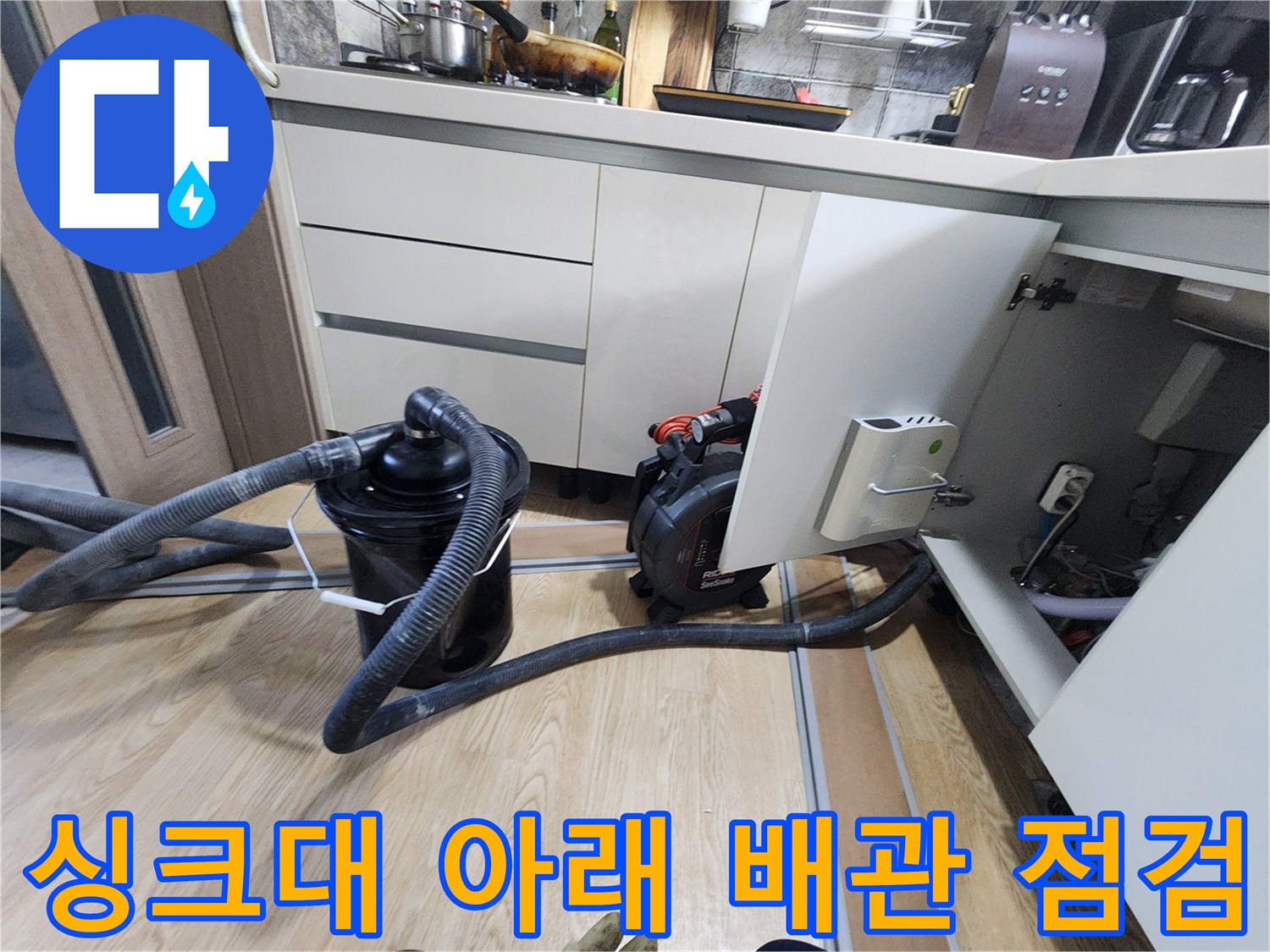 주방 싱크대 밑 공간에 배치된 배관 점검용 흡입 장비와 호스 연결 상태