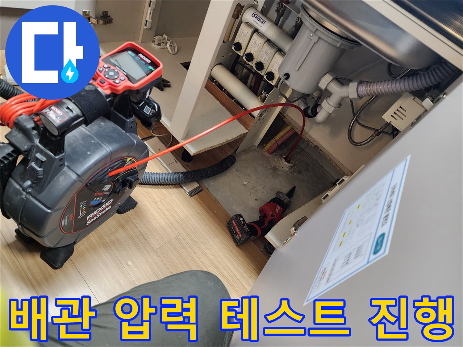 싱크대 하부장 내부에서 배관의 기밀성을 확인하기 위해 디지털 게이지를 연결하여 공압 테스트를 수행하는 모습입니다.