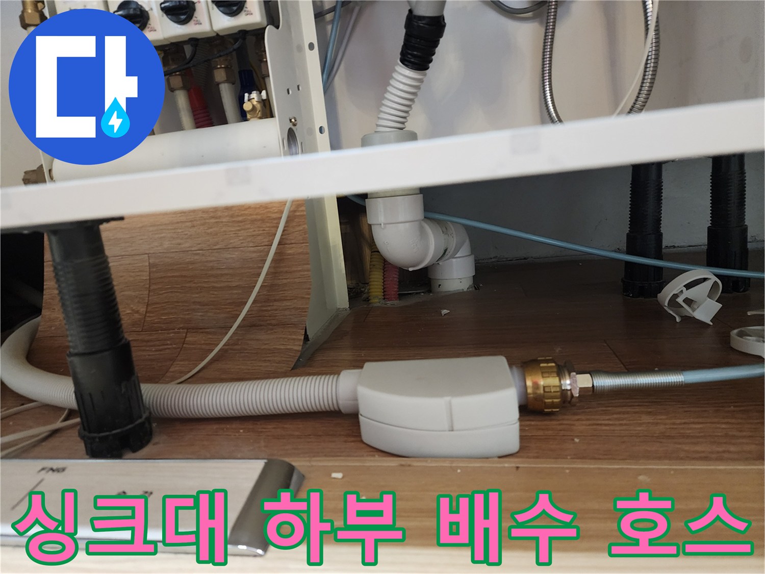 하얀색 주름관과 금속 연결 부위가 보이는 싱크대 밑 공간