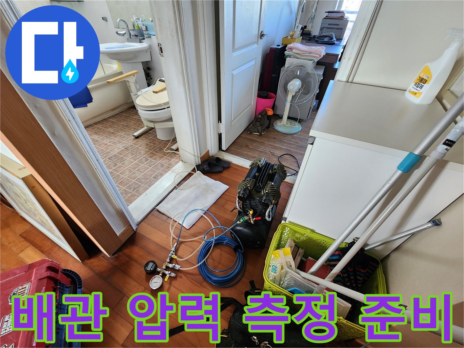 화장실 입구 바닥에 놓여 있는 누수 탐지용 공압 게이지와 호스 연결부