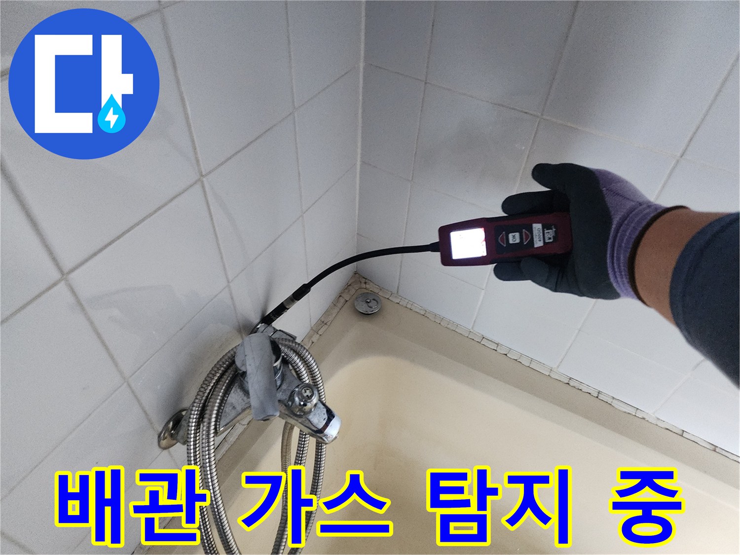 타일 벽면 사이로 연결된 배관의 누수를 찾기 위해 검측기를 사용하는 장면입니다.