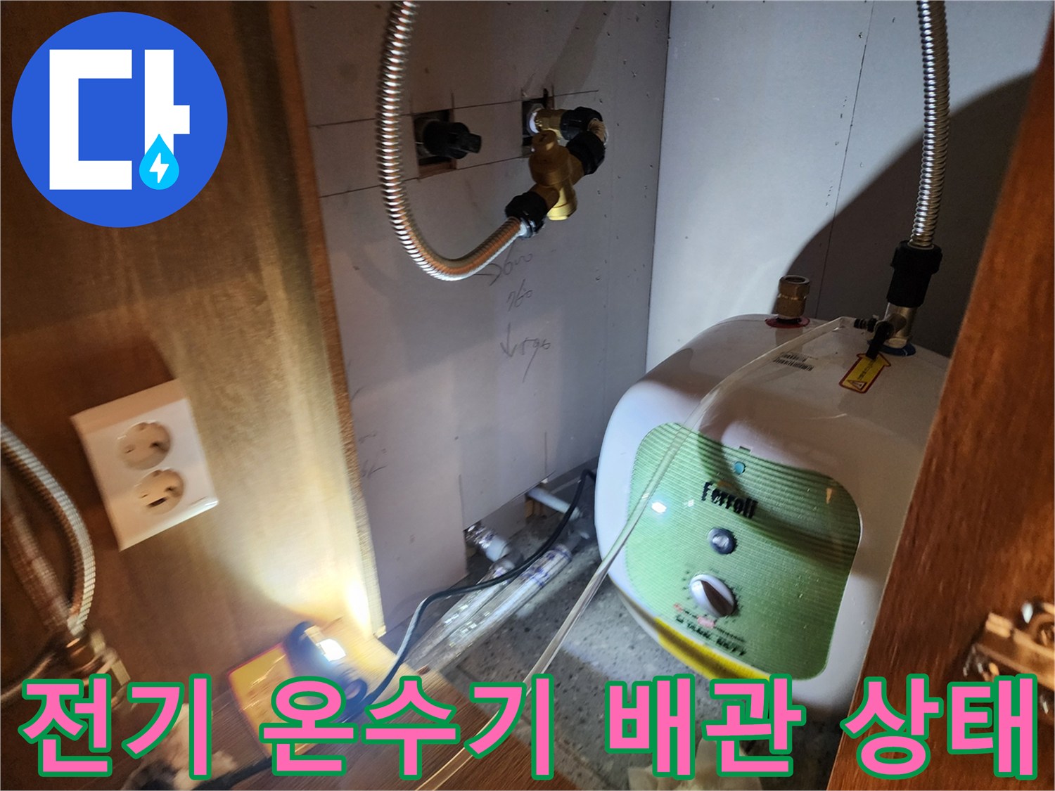 주방 하부장 내 설치된 전기 온수기와 연결 배관의 모습입니다.