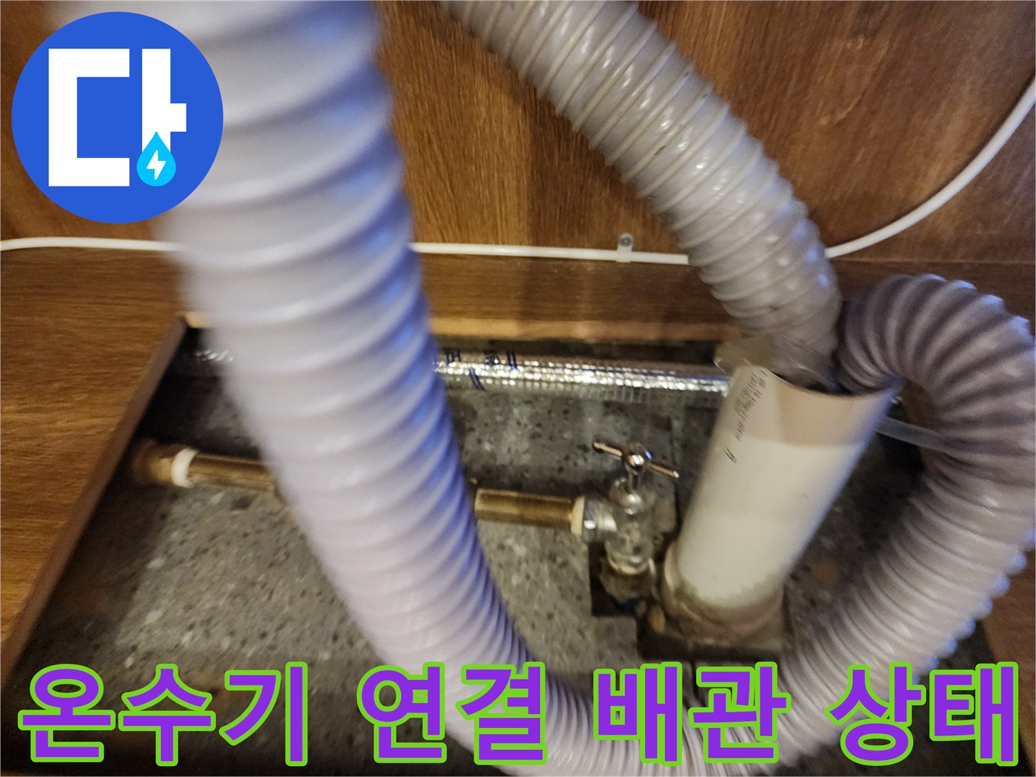 주방 하부장 내 설치된 전기 온수기와 연결된 회색 플렉시블 호스 모습
