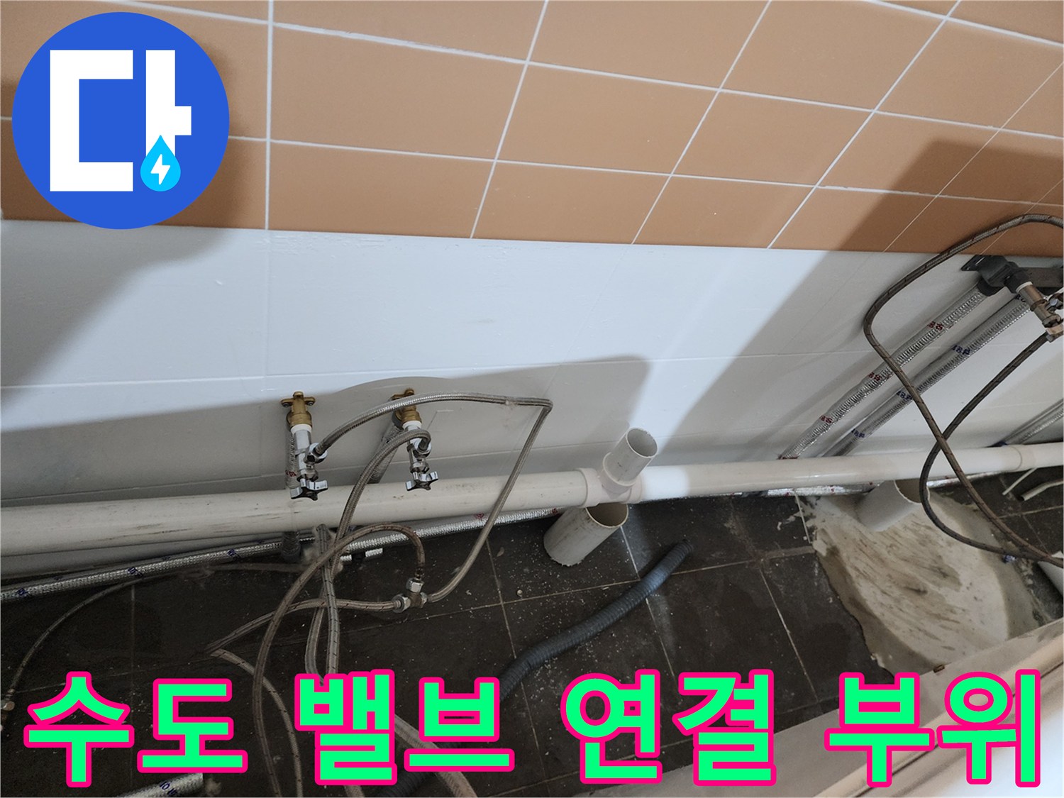 벽면 타일 아래 설치된 수도 꼭지와 호스 연결 상태를 근접 촬영했습니다.
