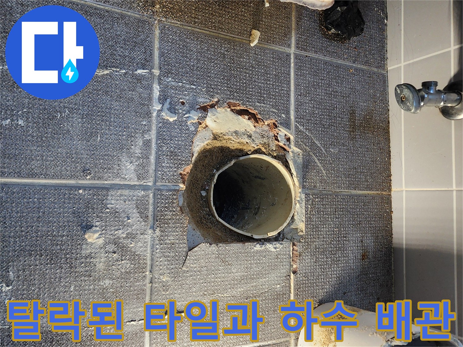 하수구 주변의 파손된 타일과 노출된 PVC 배관의 모습입니다.