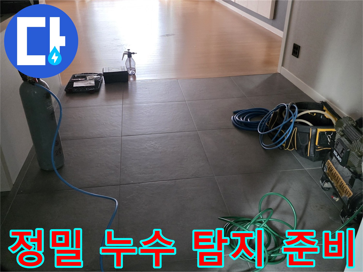 가스 탐지용 용기와 호스가 거실 바닥 타일 위에 세팅된 모습의 사진