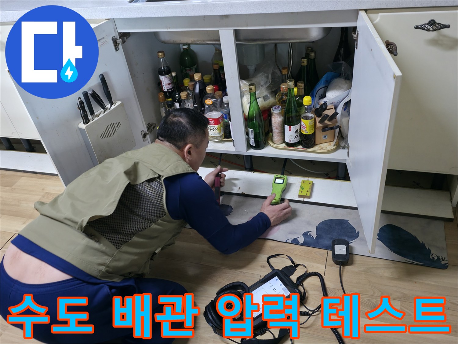 싱크대 하부 배관의 누수 여부를 판단하기 위해 압력계와 탐지기를 사용하는 장면입니다.