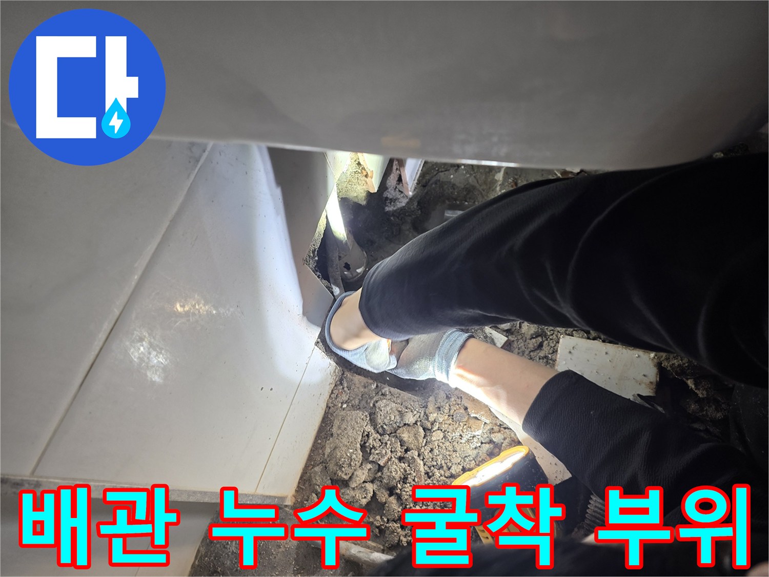 손전등 불빛에 비친 젖은 바닥 흙과 배관 주변 작업 모습