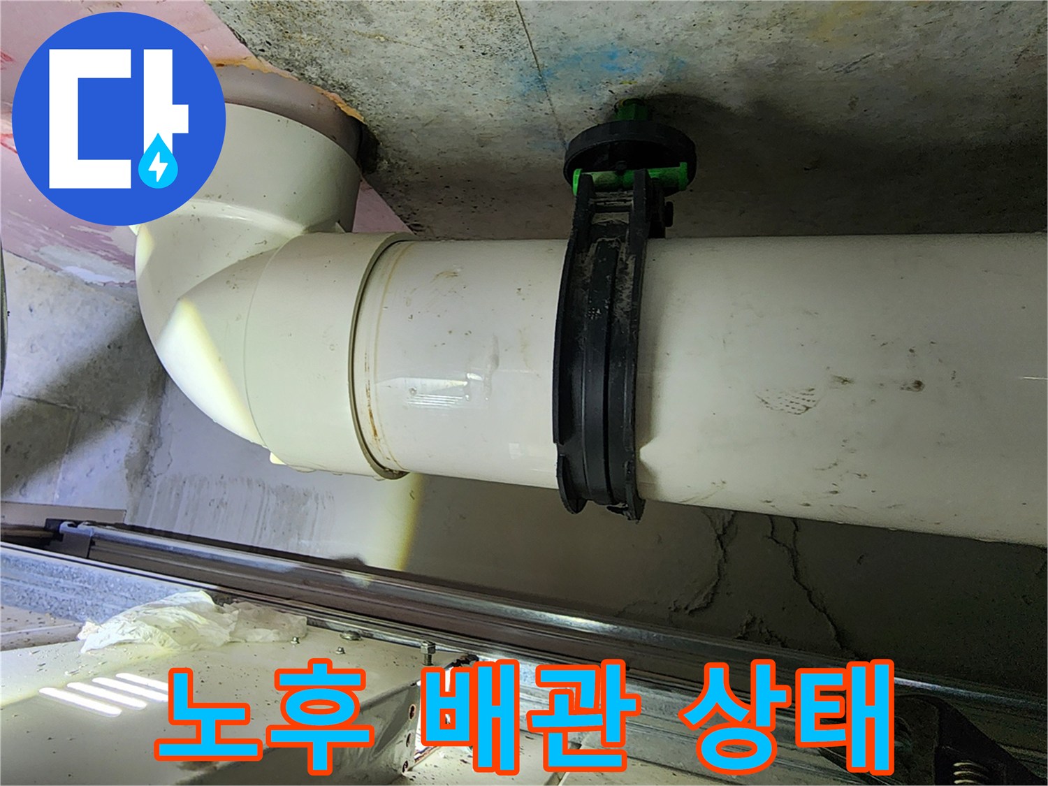 천장에 설치된 하얀색 PVC 배관과 검은색 고정 클램프 사진입니다.