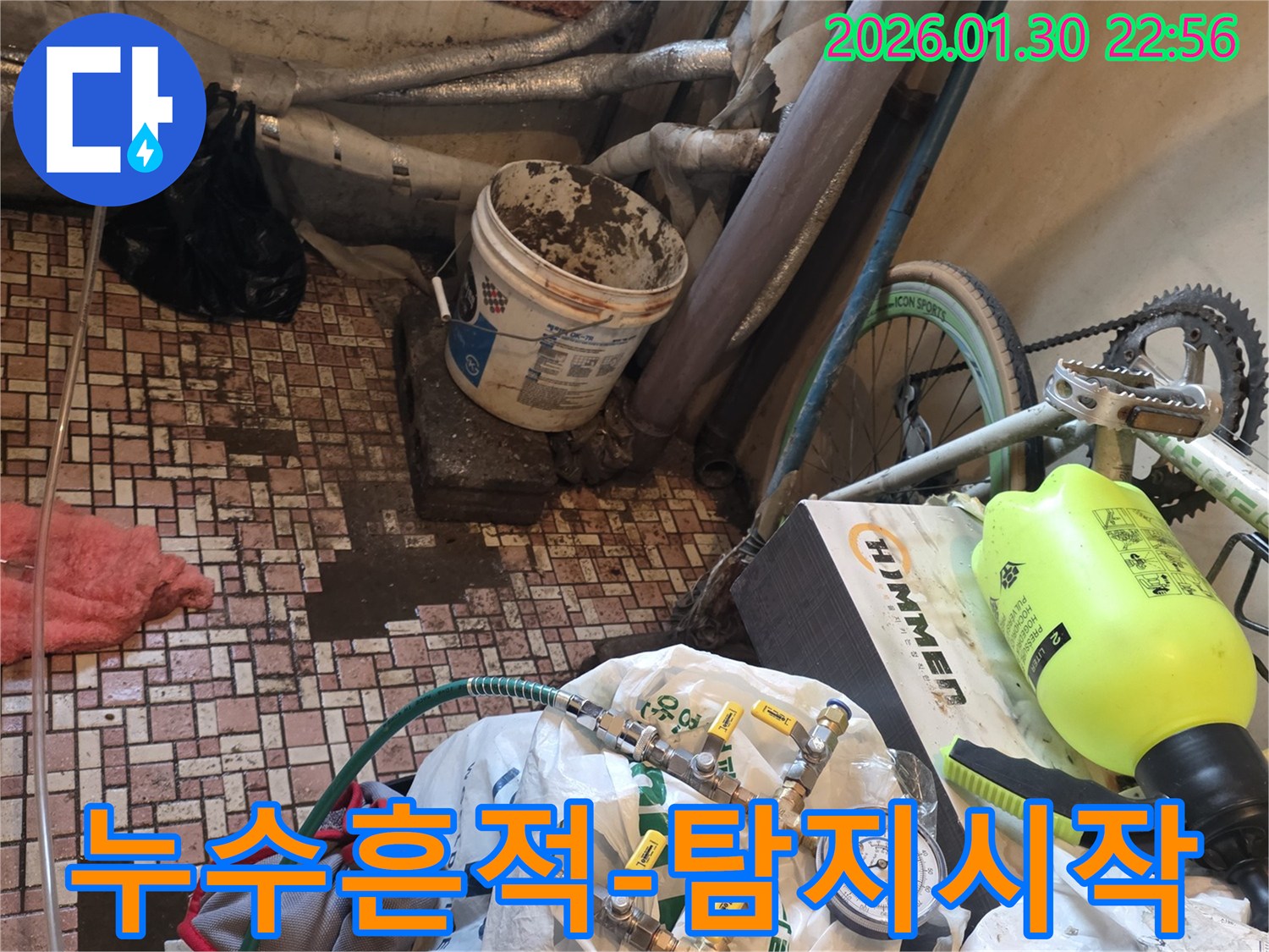 배관 누수 지점을 찾기 위해-압력 게이지와 호스가 연결된-전문 탐지 장비가 사용되는 장면입니다.
