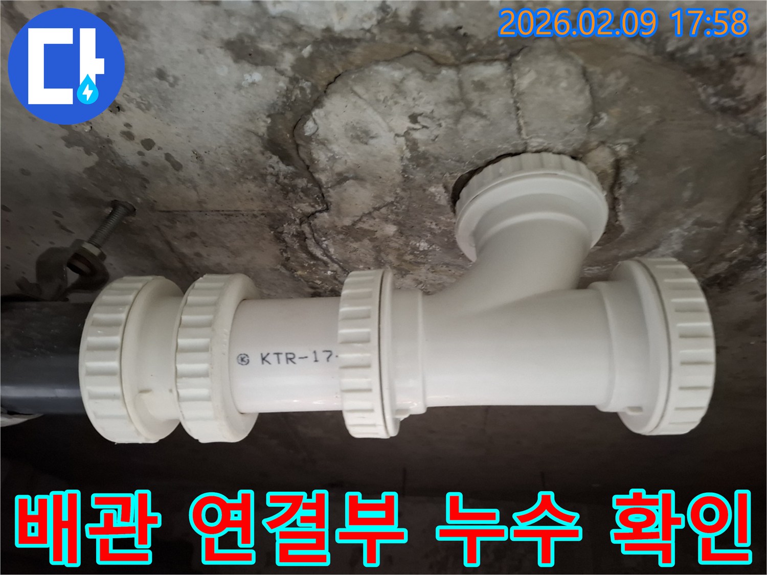 손상된 콘크리트 천장 아래-새로운 배관 연결부가 보이는 모습-누수로 인한 얼룩이 선명합니다.