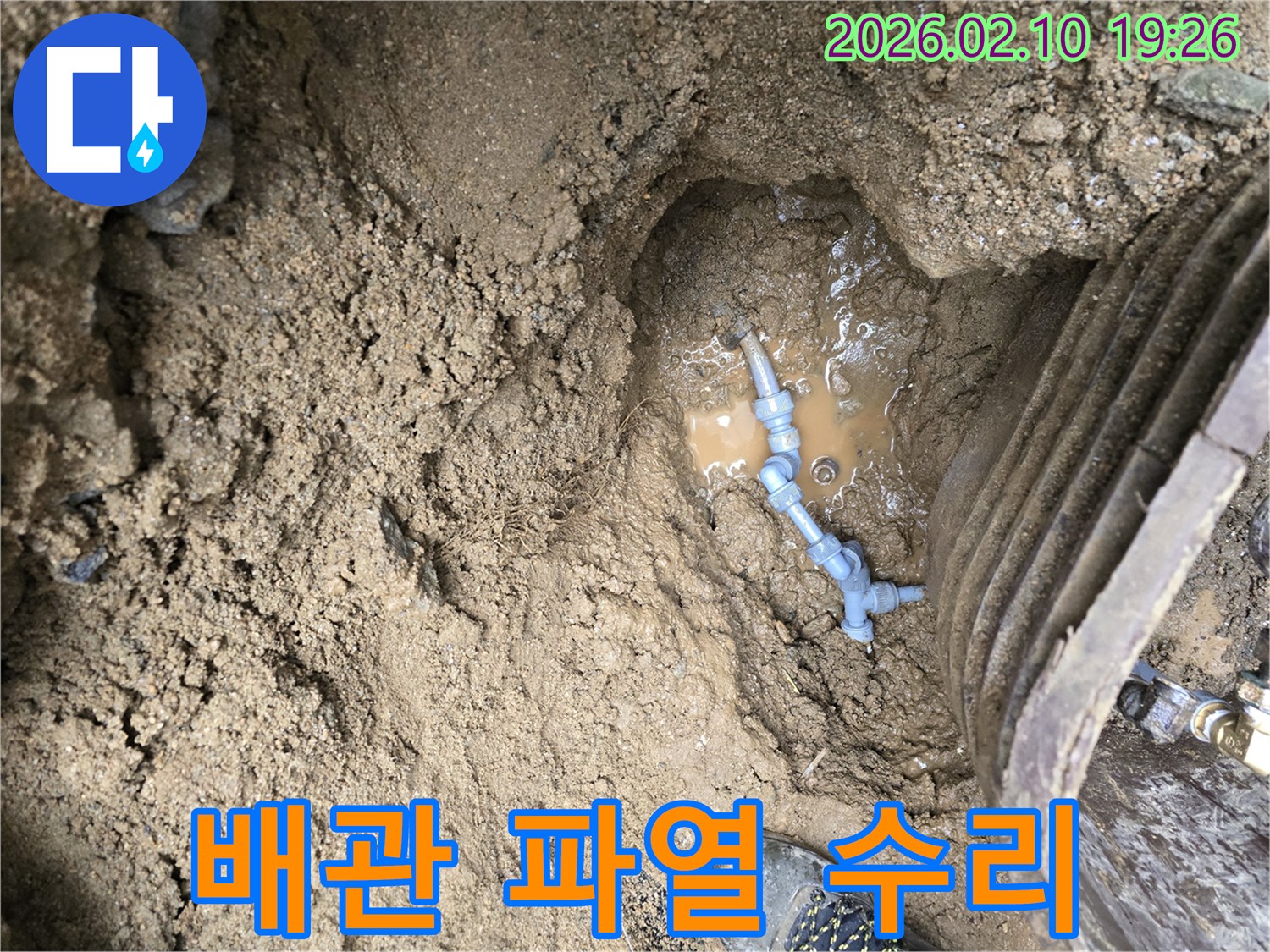 흙 속에 묻힌 수도배관이 파열되어-물이 고여있는 누수 현장을 보여주는 사진입니다