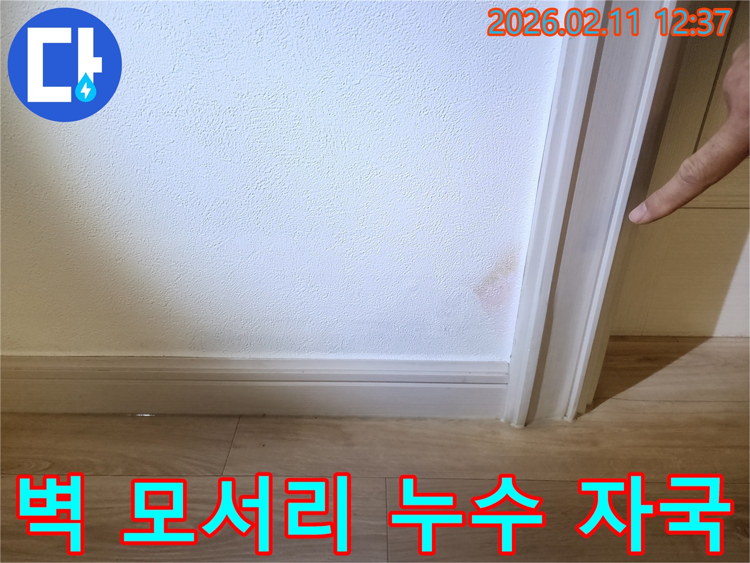벽면 모서리 하단에 발생한 물자국은- 누수로 인해 벽지가 젖고 변색된 상태를 보여줍니다.
