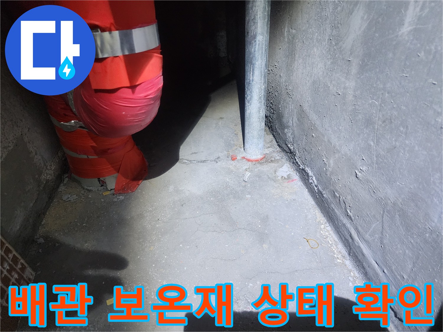 붉은색 보온재가 씌워진 배관과 회색 벽면의 연결 부위 사진입니다.