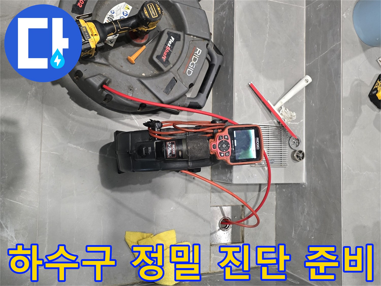 욕실 바닥에 배치된 배관 점검용 카메라와 전동 드릴 및 석션 장비