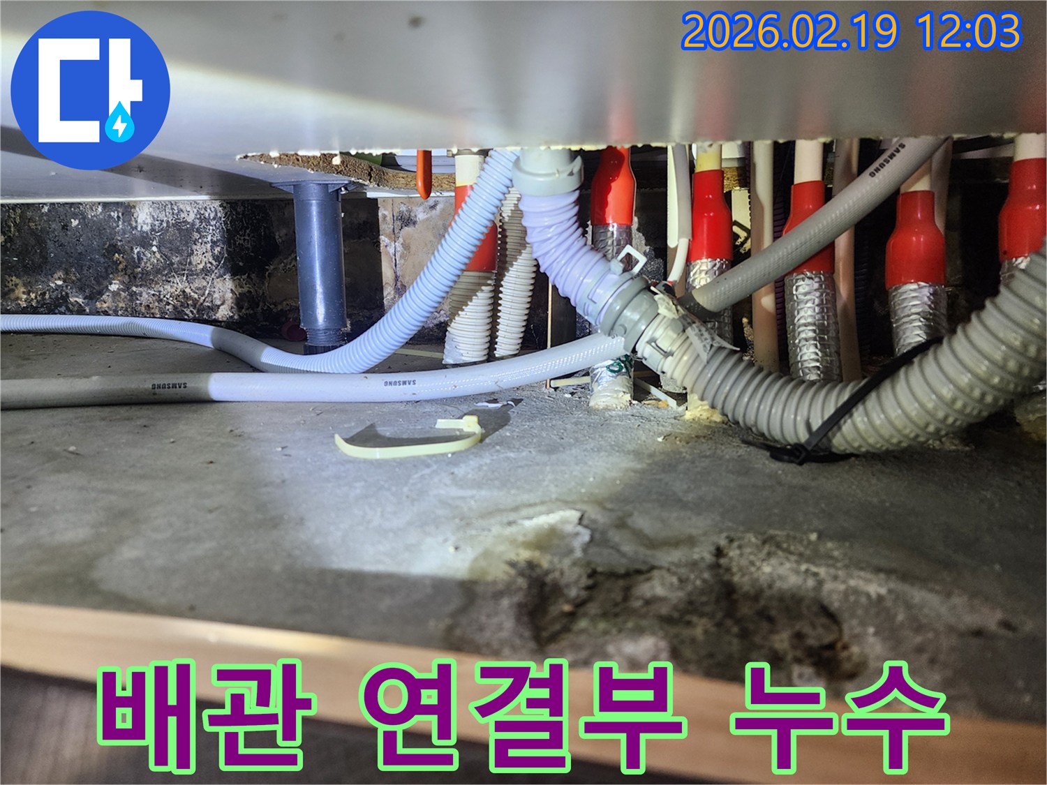 싱크대 하부의 복잡한 배관 연결부에서-물이 새어 나와-주변이 젖어있는 모습을 보여주는 사진입니다