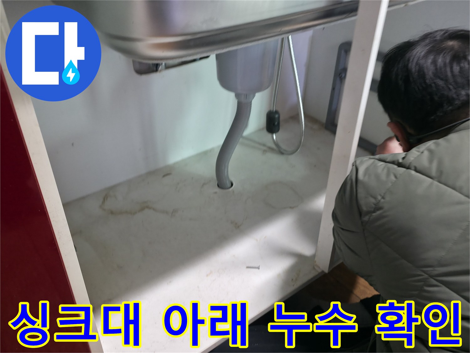 주방 싱크대 하부장 내부의 은색 주름관과 배관 연결 상태를 점검하는 엔지니어