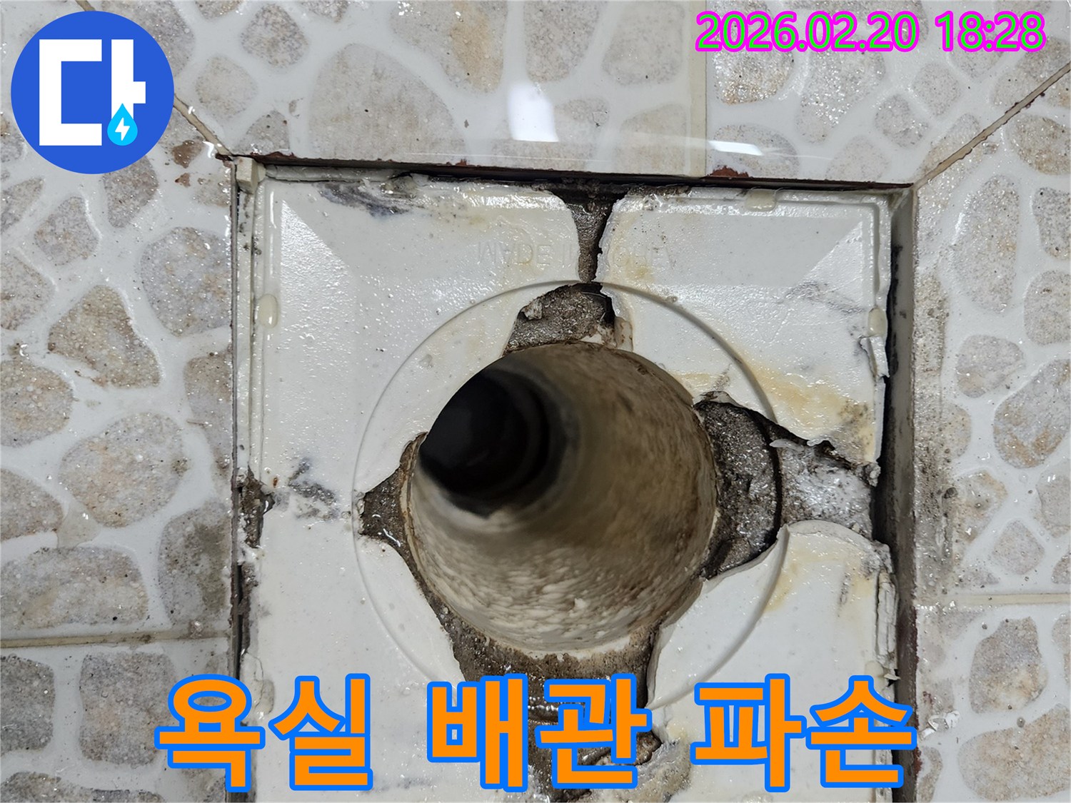 이 이미지는-욕실 배수구의 심각한 파손으로-배관이 노출되고-주변 방수층이 손상되어-물이 새는 현장을-보여주고 있습니다