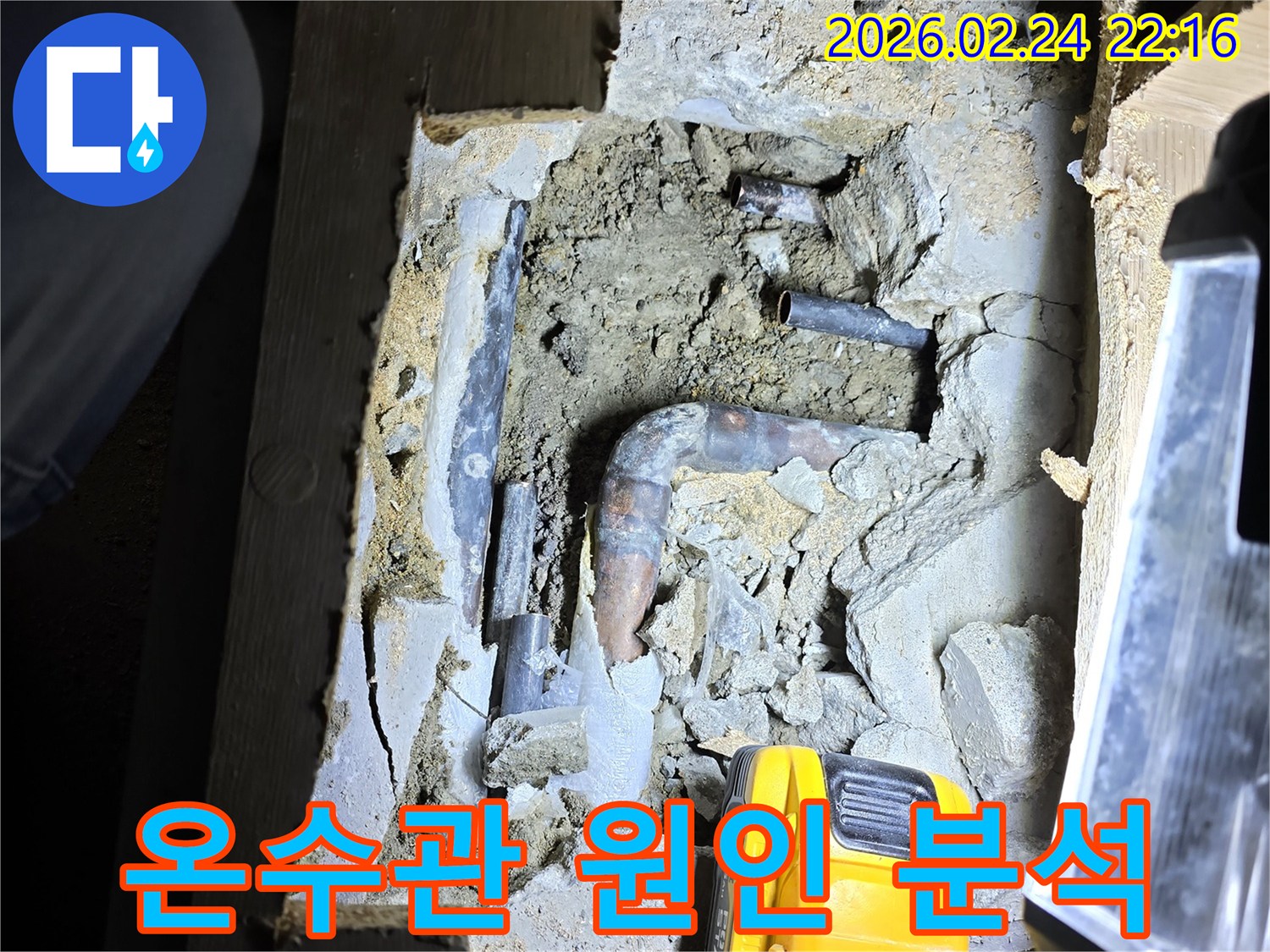 어두운 공간에서-손전등으로 비추며-오래된 온수 배관의-누수 지점을-첨단 장비로 확인하고-원인 분석을-준비하는 모습입니다.