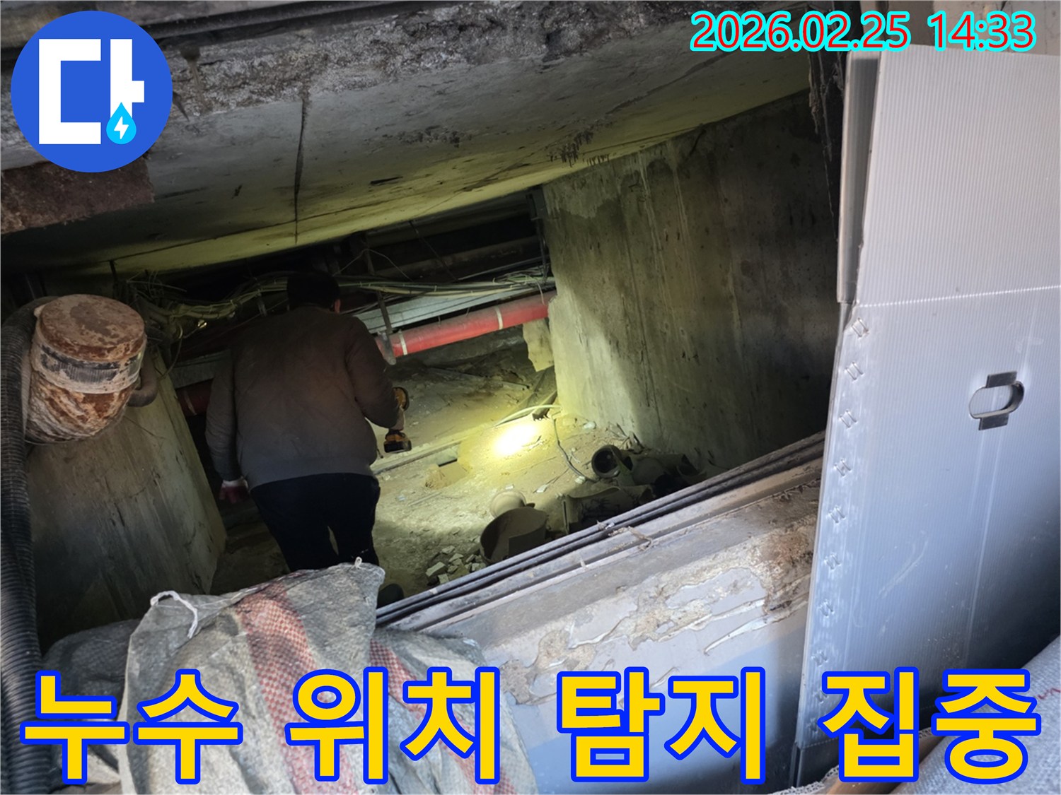 누수 전문 엔지니어가-어둡고 좁은 공간에서-손전등을 비춰가며-누수 발생의 정확한 위치를-탐지하기 위해-집중하는 모습입니다.