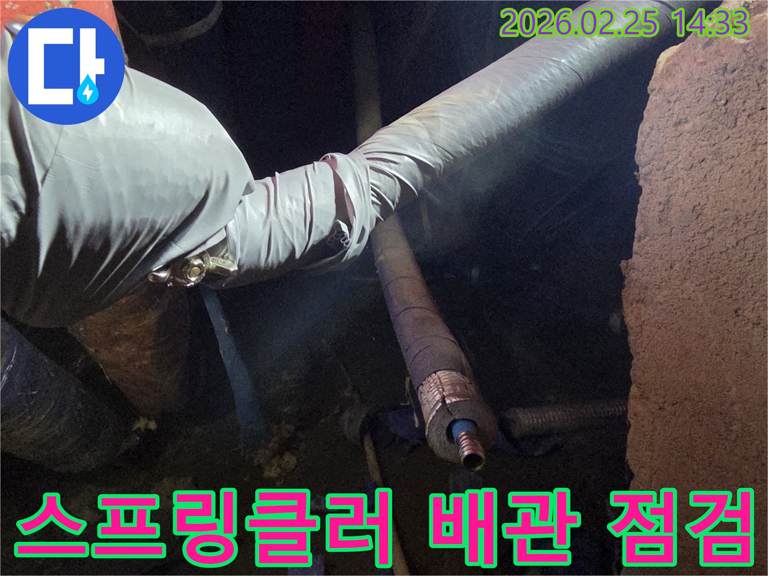어두운 작업 공간에서-장갑을 낀 손이-스프링클러 배관의-손상된 연결 부위를-세심하게 점검하며-누수 여부를-확인하는 모습입니다