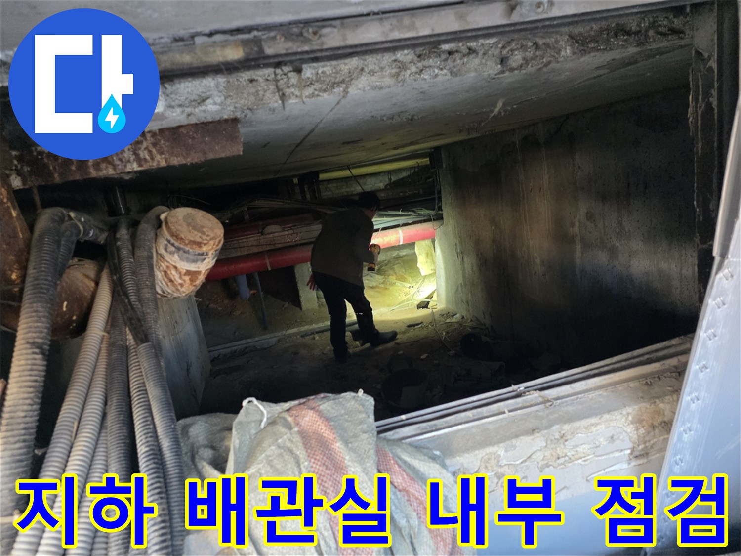 어두운 지하 배관실 공간에서 작업자가 천장 배관 상태를 확인하고 있습니다.