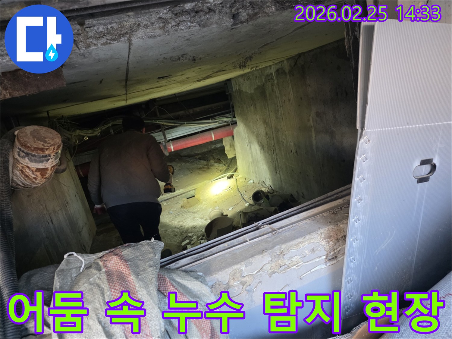 전문 누수 엔지니어가-어두운 지하 공간에서-손전등 불빛에 의지하여-배관의 미세한 누수 지점을-정확히 찾아내기 위해-집중적으로 탐사하는 모습입니다.