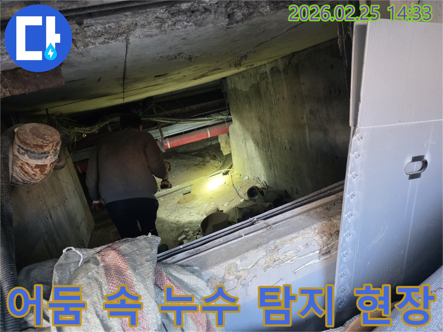 전문 누수 엔지니어가-어두운 지하 공간에서-손전등 불빛에 의지하여-배관의 미세한 누수 지점을-정확히 찾아내기 위해-집중적으로 탐사하는 모습입니다.