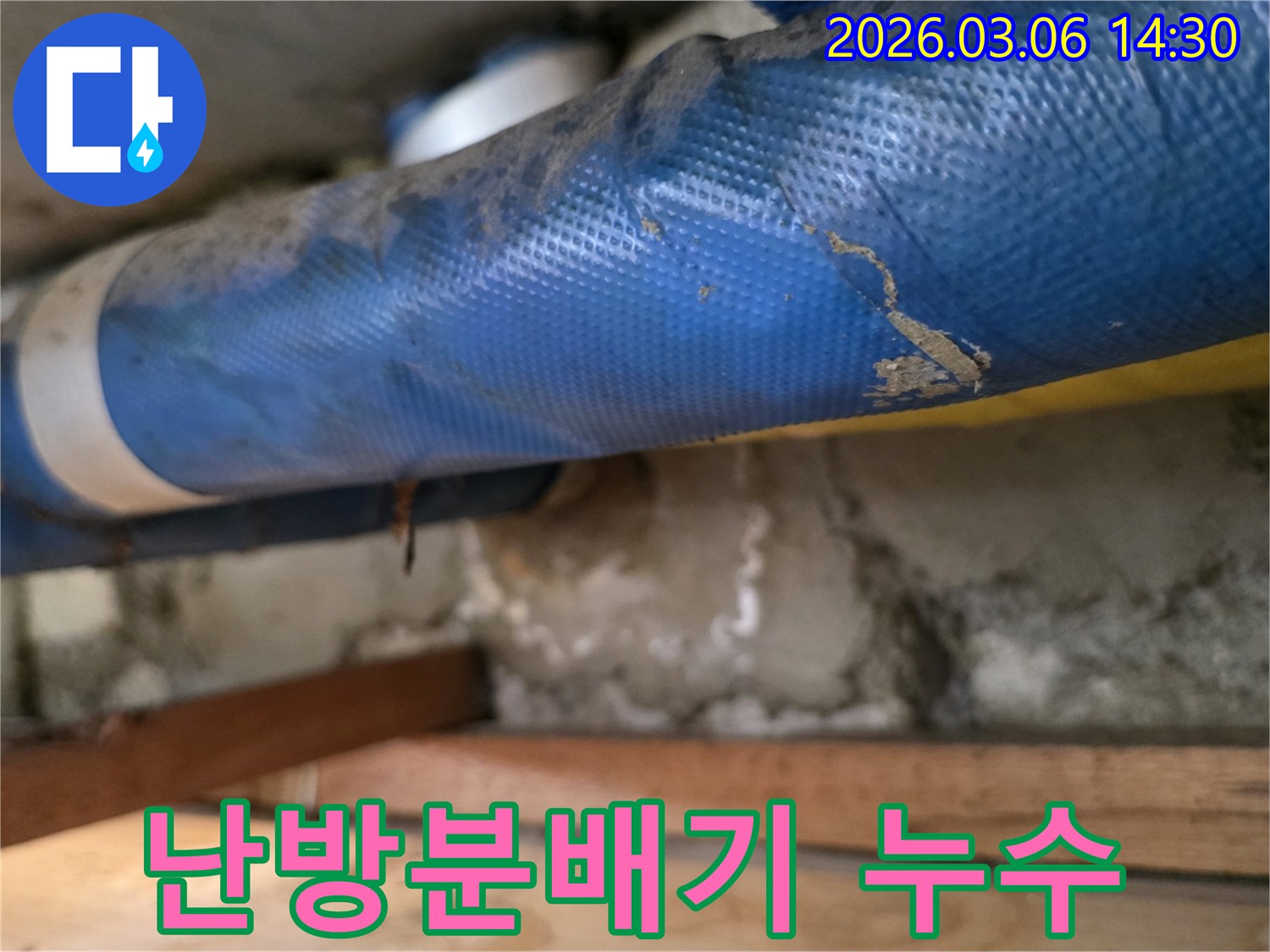 빌라 난방분배기 하부-파란색 배관과-젖은 콘크리트 벽면-그리고 나무 지지대를-꼼꼼히 점검하는 모습