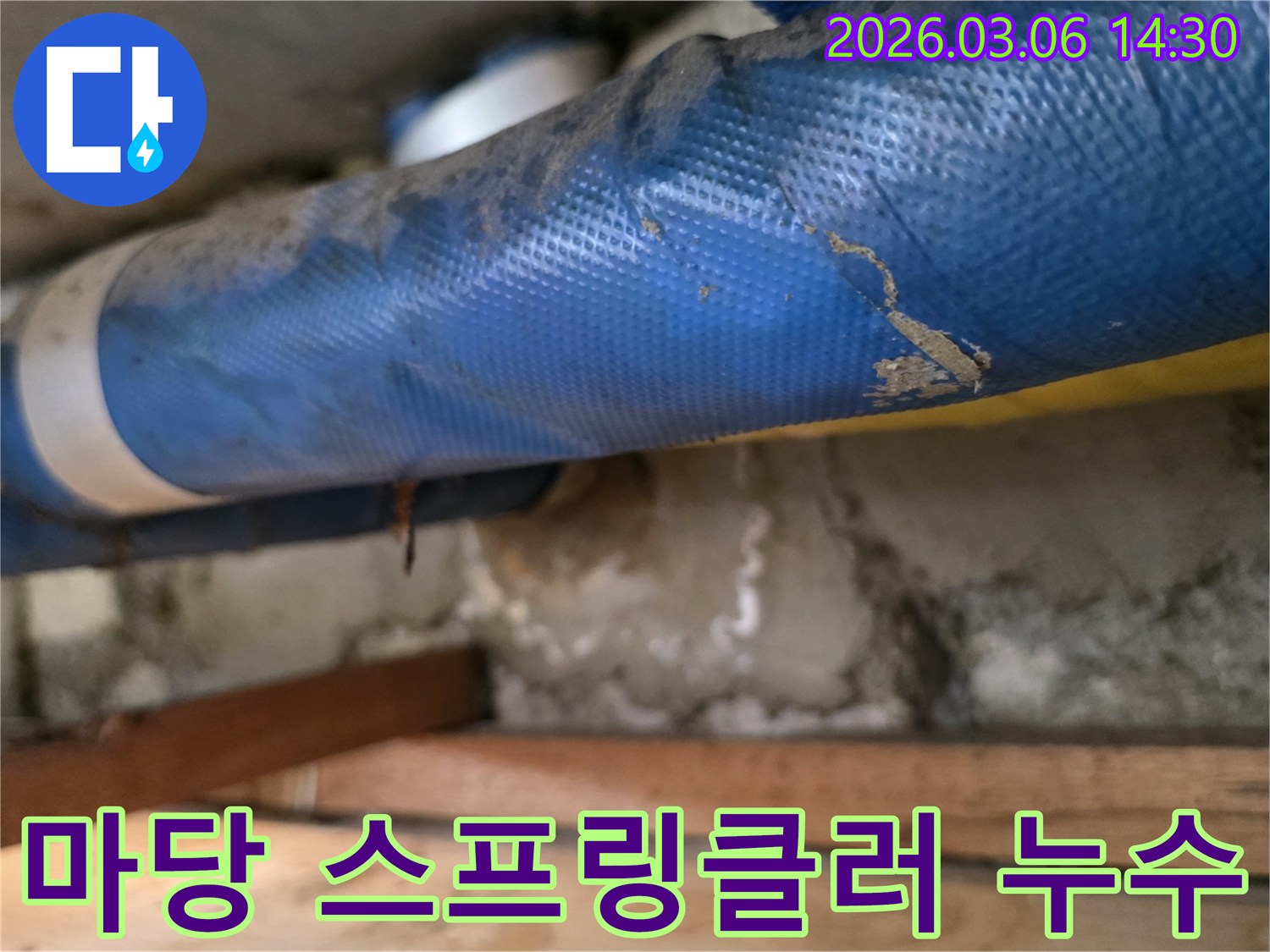 주택 마당 하부-파란색 스프링클러 배관과-젖은 흙벽면-그리고 나무 지지대를-정밀하게 점검하는 모습