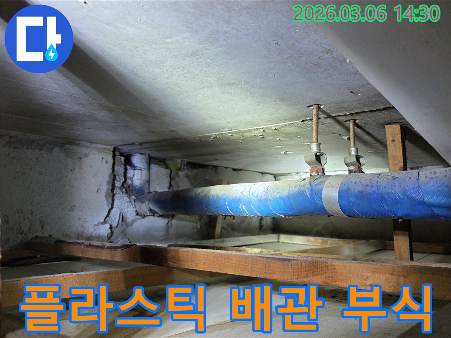지하 공간의 낡은-파란색 플라스틱 배관과-그로 인해 손상된 콘크리트 벽면을-누수 엔지니어가-배관의 부식 상태를-점검하는 모습