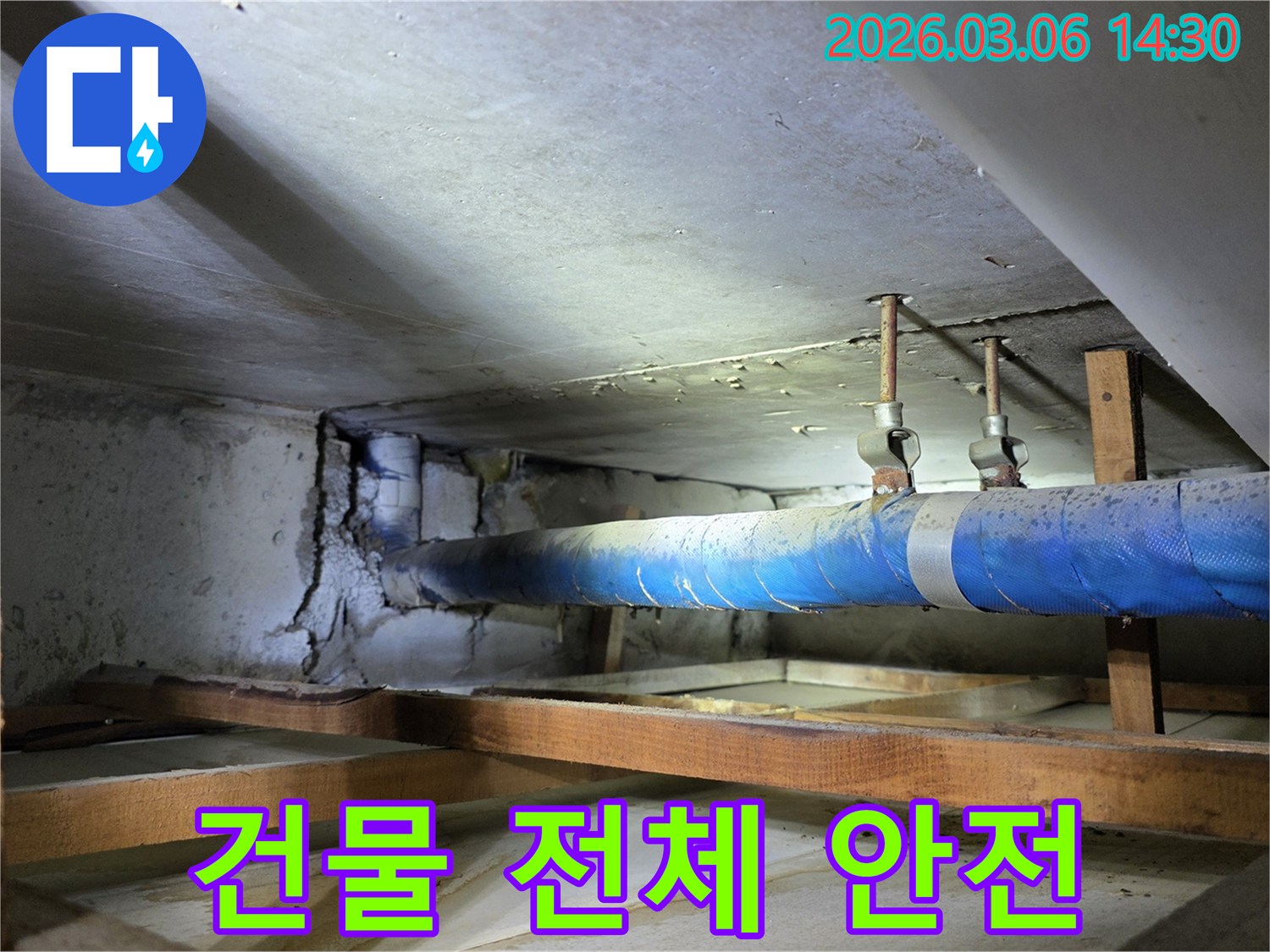 지하 공간의 파란색 배관과-손상된 콘크리트 벽면을-누수 엔지니어가-건물 전체 안전 점검을 위해-정밀하게 살피는 모습