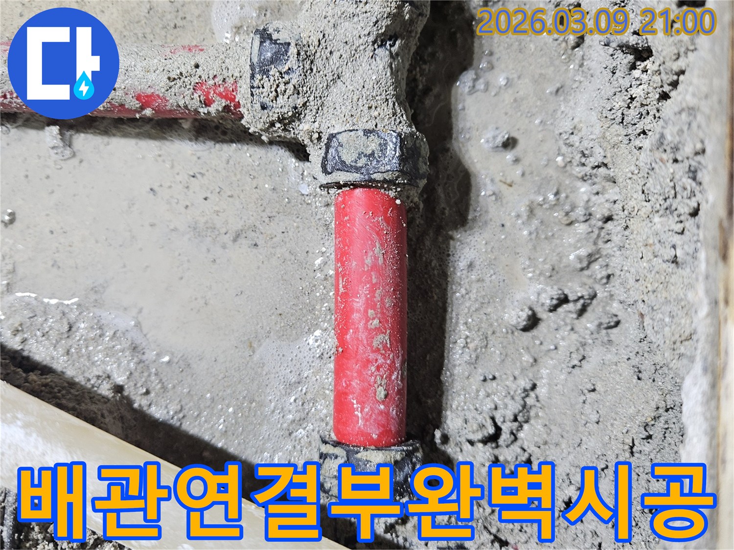 젖은 시멘트 바닥에-매립된 빨간색 배관의-연결 부위가-틈새 없이-완벽하게 시공된-모습입니다