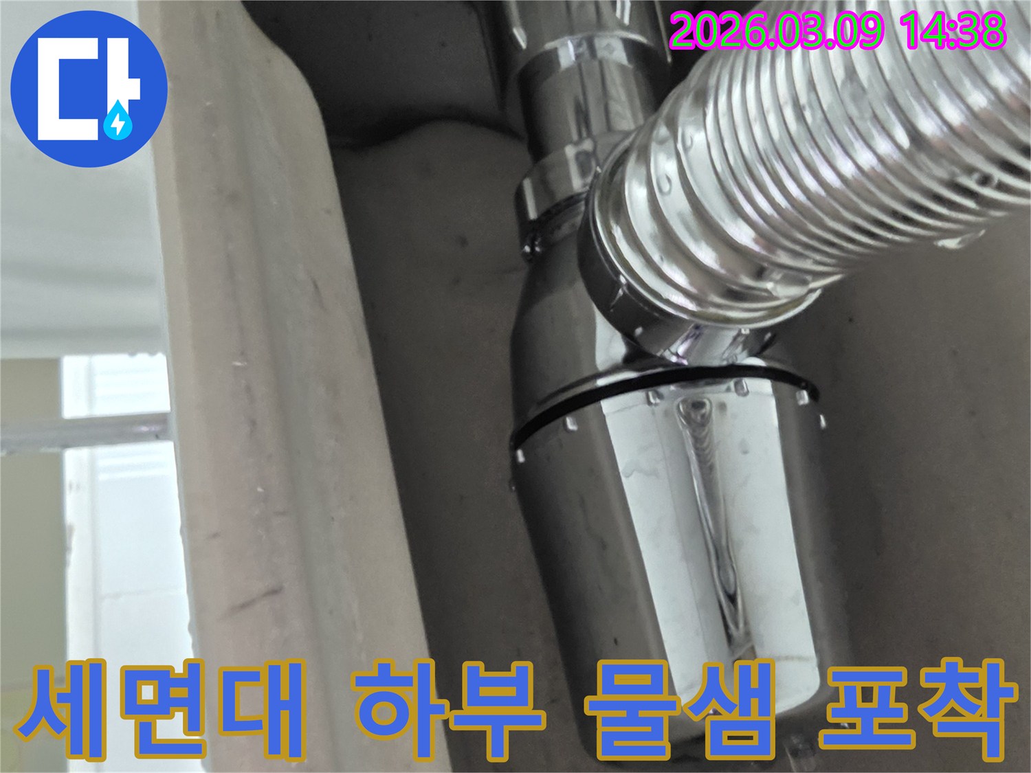 이 사진은 세면대 하부 배수관의 연결 부위에서 물이 새는-누수 지점을 명확히 보여줍니다