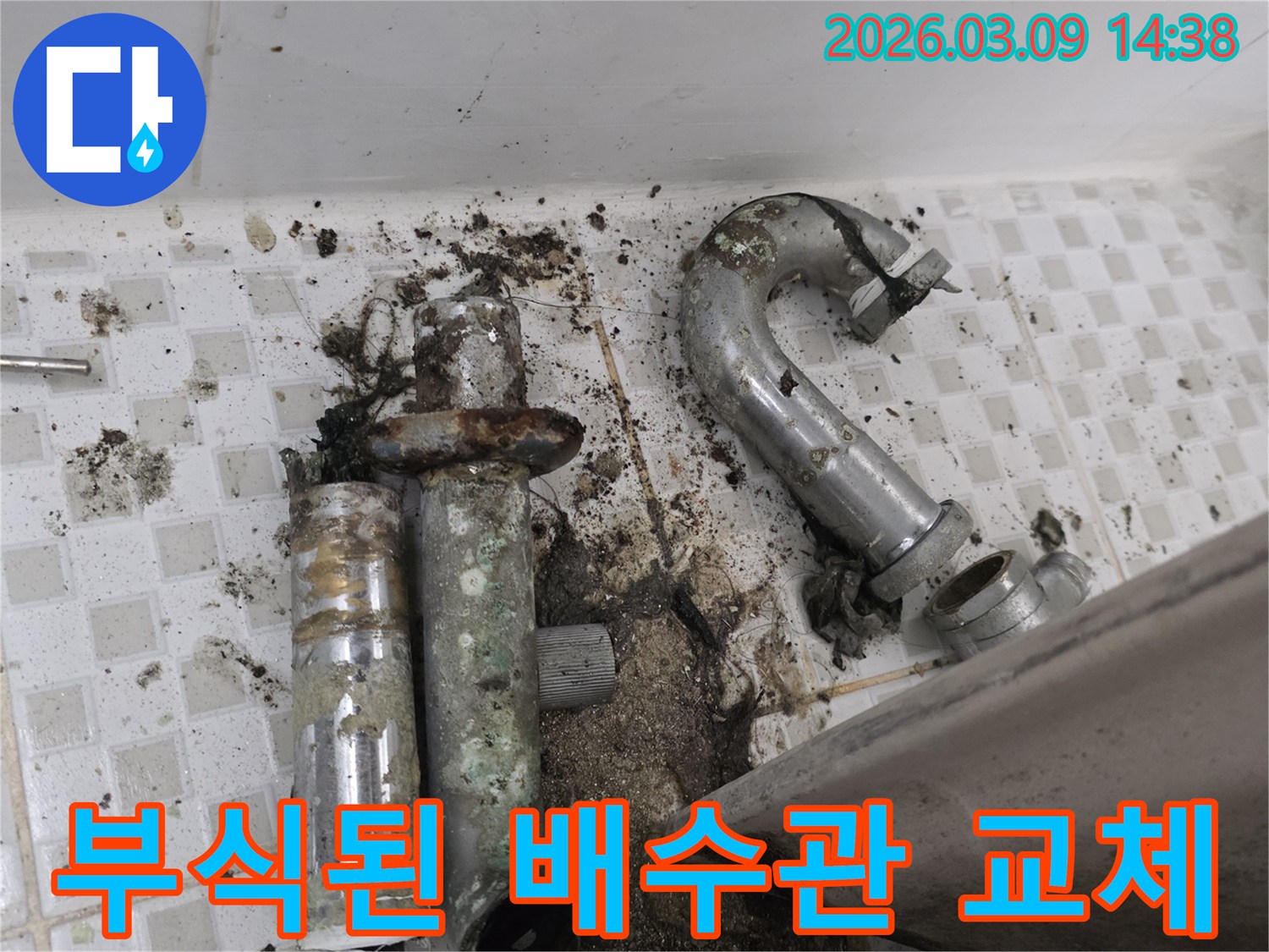 이 이미지는 욕실 바닥에 심각하게 부식되어 파손된 배수관과-주변의 오염된 타일을 보여주며-누수 공사 전의 상태를 나타냅니다