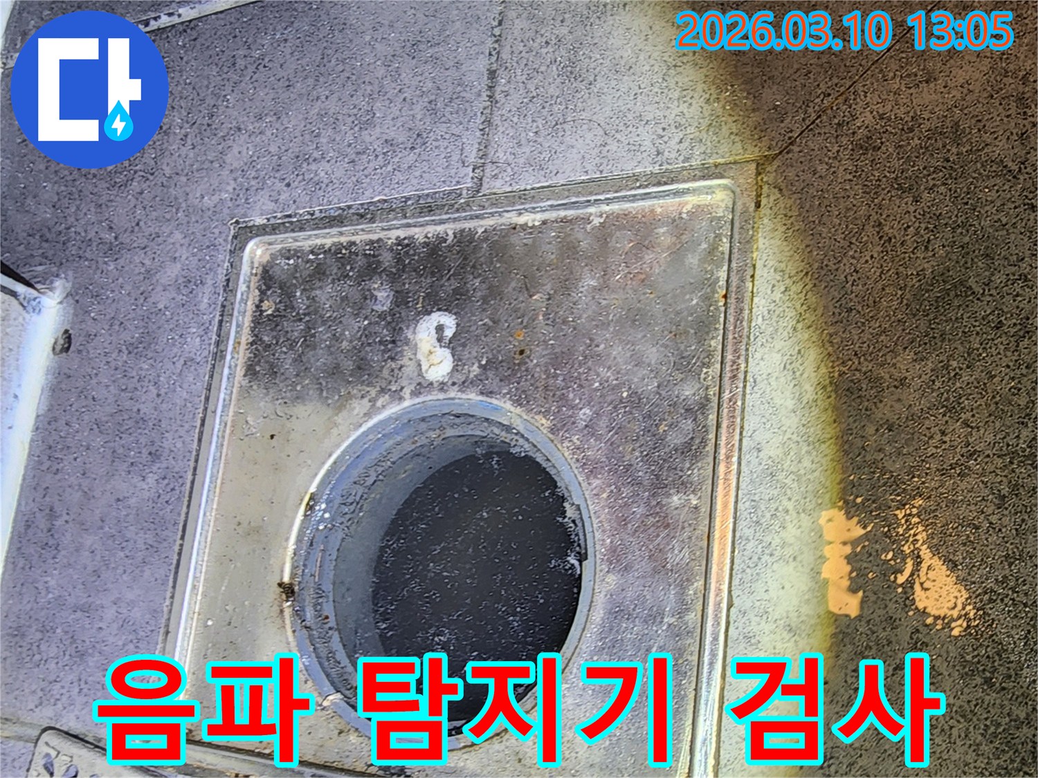 누수 엔지니어가 바닥 배수구 하부의 배관에서 발생하는 미세한 누수음을 감지하기 위해-음파 탐지기를 활용한 검사를 준비하는 모습입니다