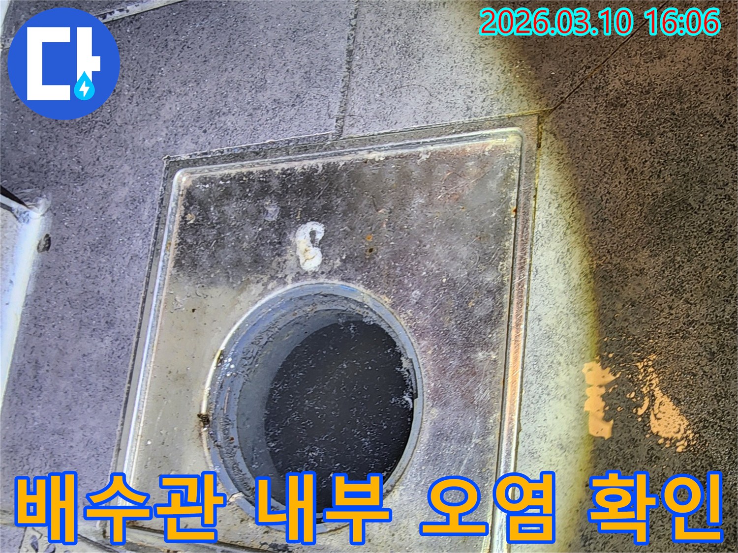 이 이미지는-서울 중구의 한 건물에서-누수 원인을 찾기 위해-배수구 커버를 열고-배수관 내부의 오염 및-손상 상태를-면밀히 확인하는-현장을 촬영한 것입니다