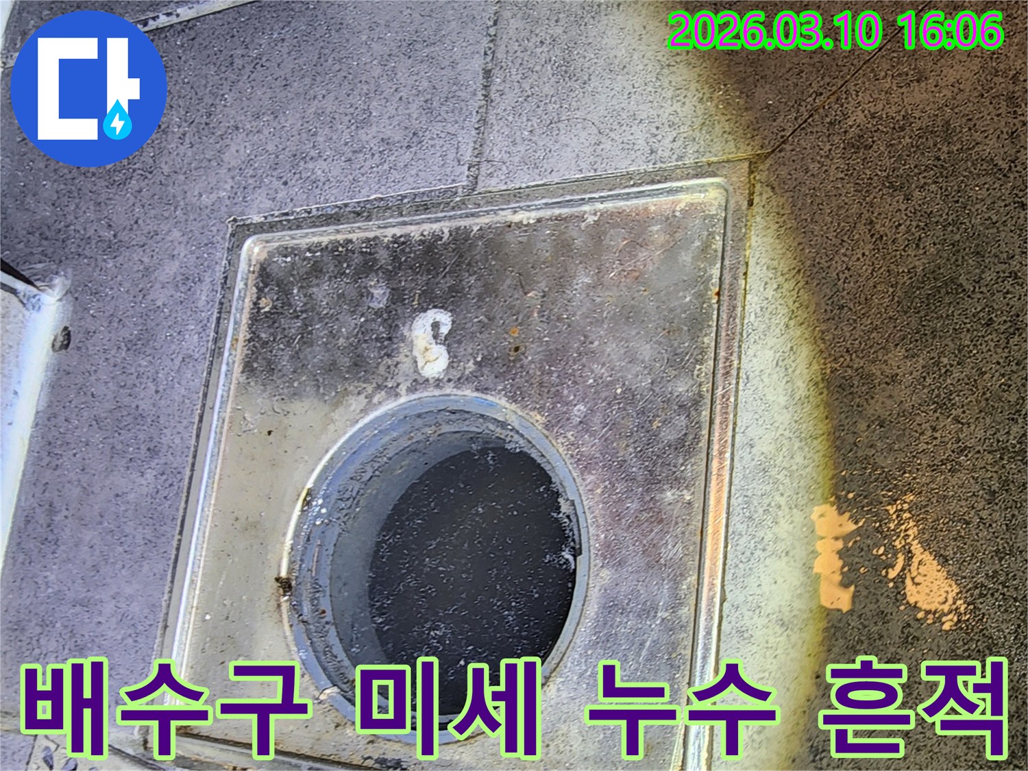 이 이미지는-서울 중구의 한 건물에서-누수 탐지 전문가가-배수구 주변의-육안으로 확인하기 어려운-미세 누수 흔적을-발견하고-정밀하게 분석하는-현장을 보여줍니다
