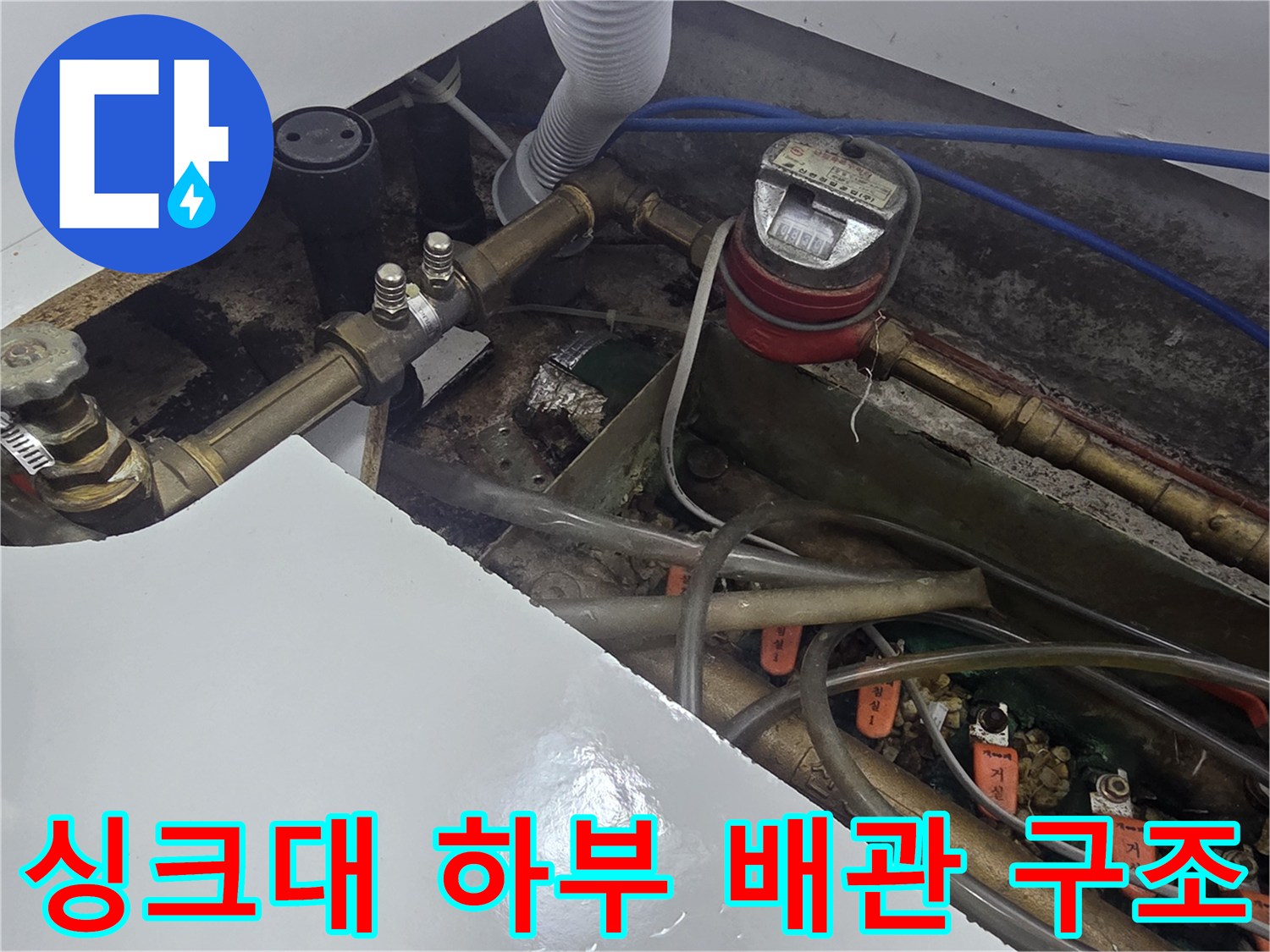 싱크대 아래 수도 계량기와 연결된 여러 갈래의 배관 및 호스